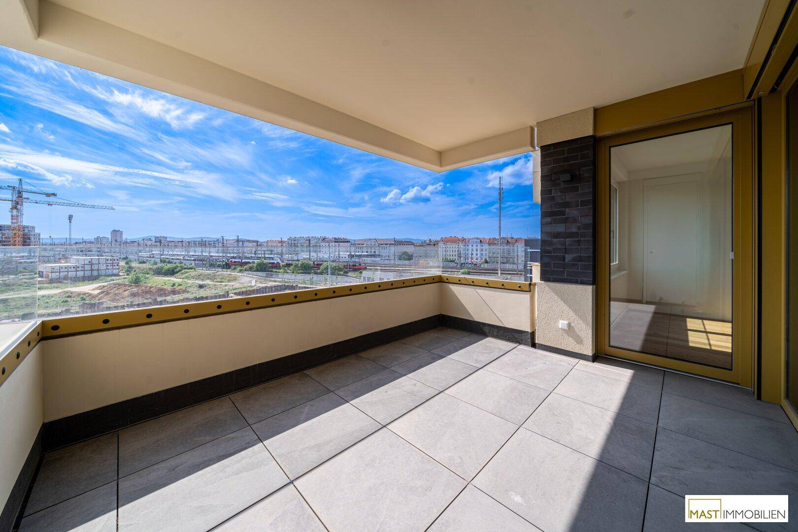 Großer Balkon mit Fliesenboden und moderner Glasbrüstung, bietet einen weiten Stadtblick.