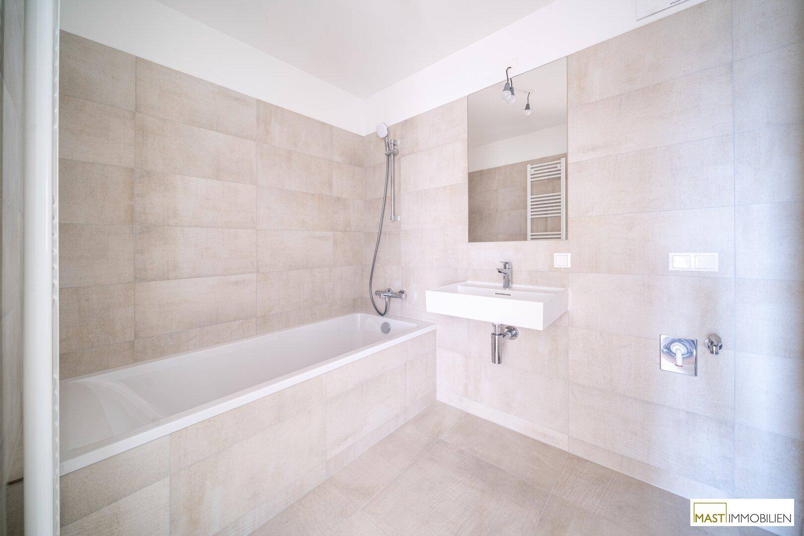 Modernes Badezimmer mit hellen Fliesen, Badewanne, wandmontiertem Waschbecken und Handtuchheizkörper.