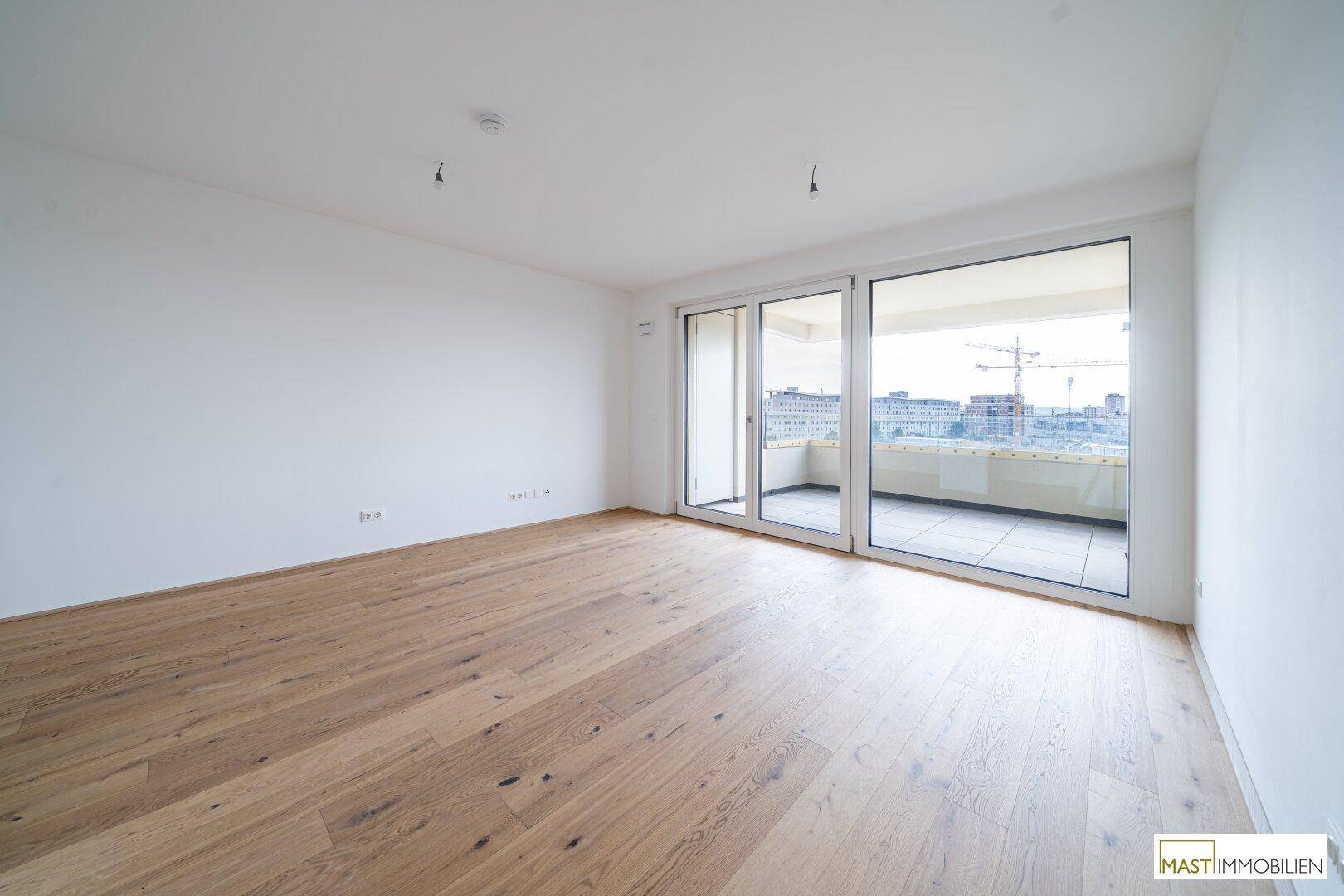 Geräumiger, unmöblierter Raum mit hellem Holzboden und direktem Zugang zu einem Balkon.