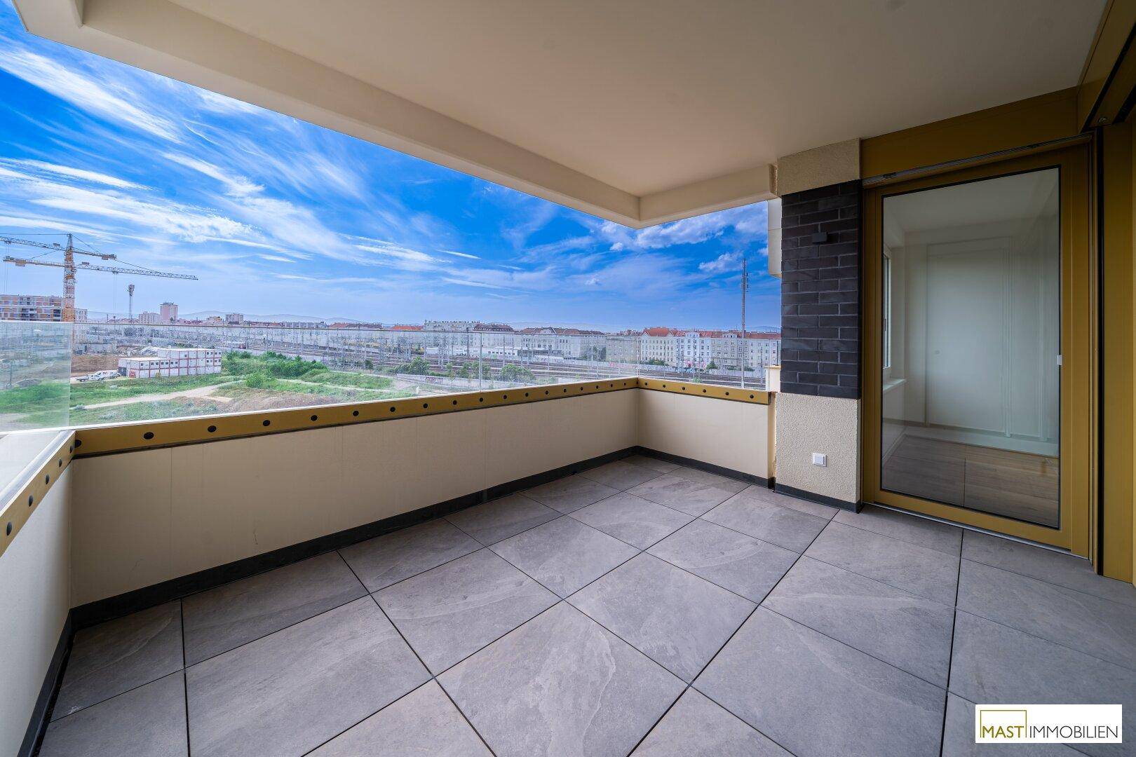 Moderner Balkon mit Fliesenboden und Glasgeländer, bietet einen weiten Blick über die städtische Umgebung.