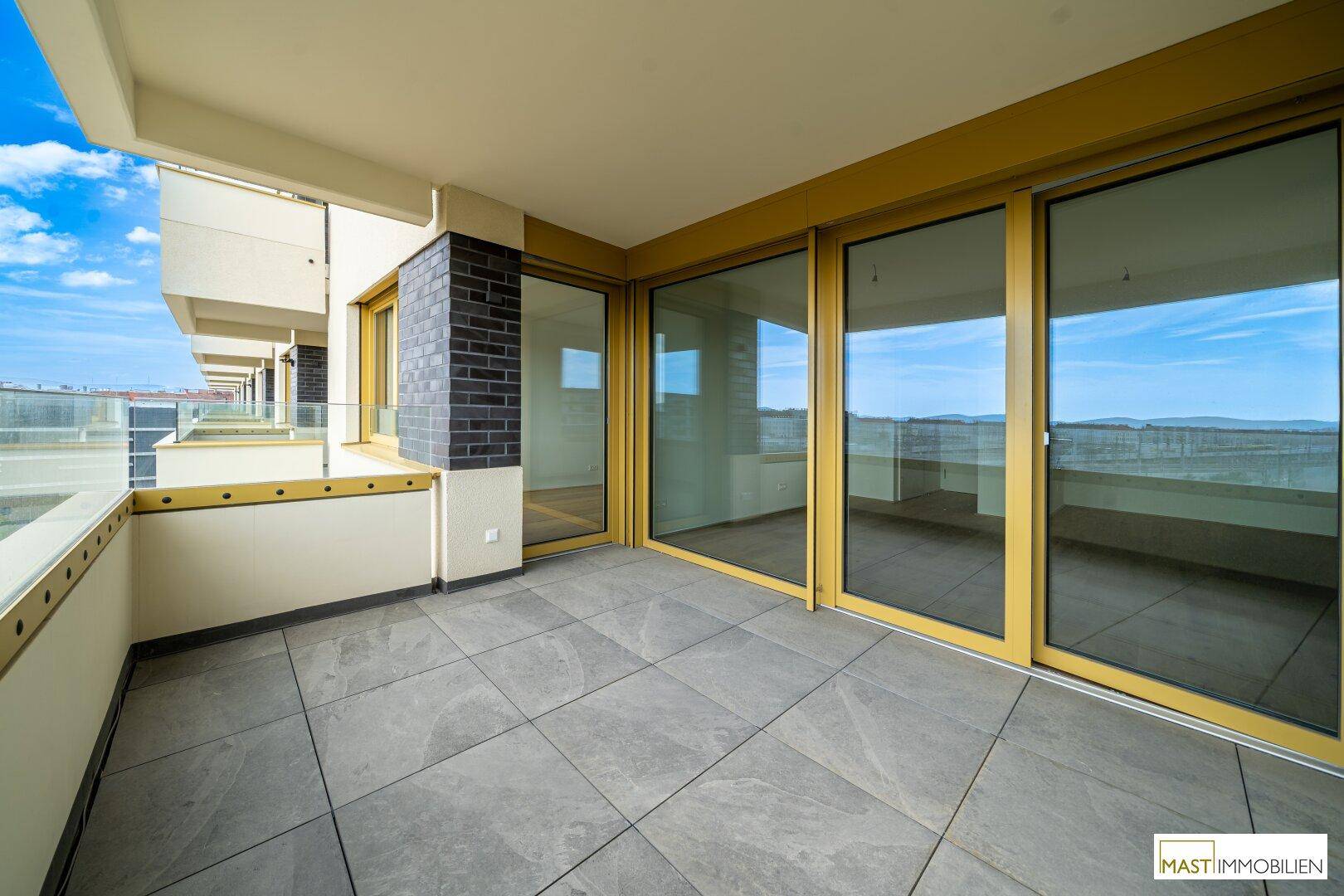 Heller Balkon mit Fliesenboden und großen Glasschiebetüren, die Zugang zu den Innenräumen bieten.