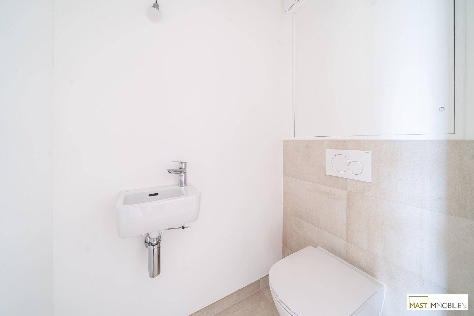 Separates Gäste-WC mit wandhängender Toilette und kleinem Handwaschbecken.