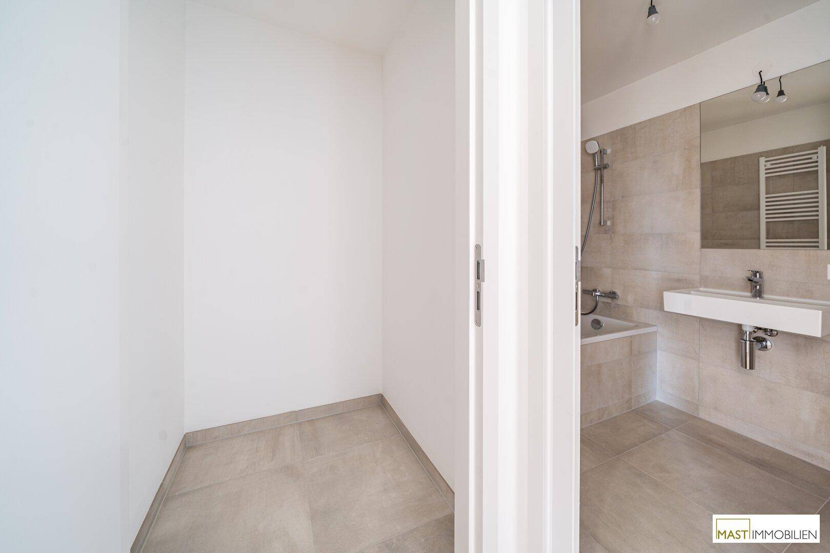 Modernes Badezimmer mit Badewanne, Waschbecken und angrenzendem Abstellbereich.