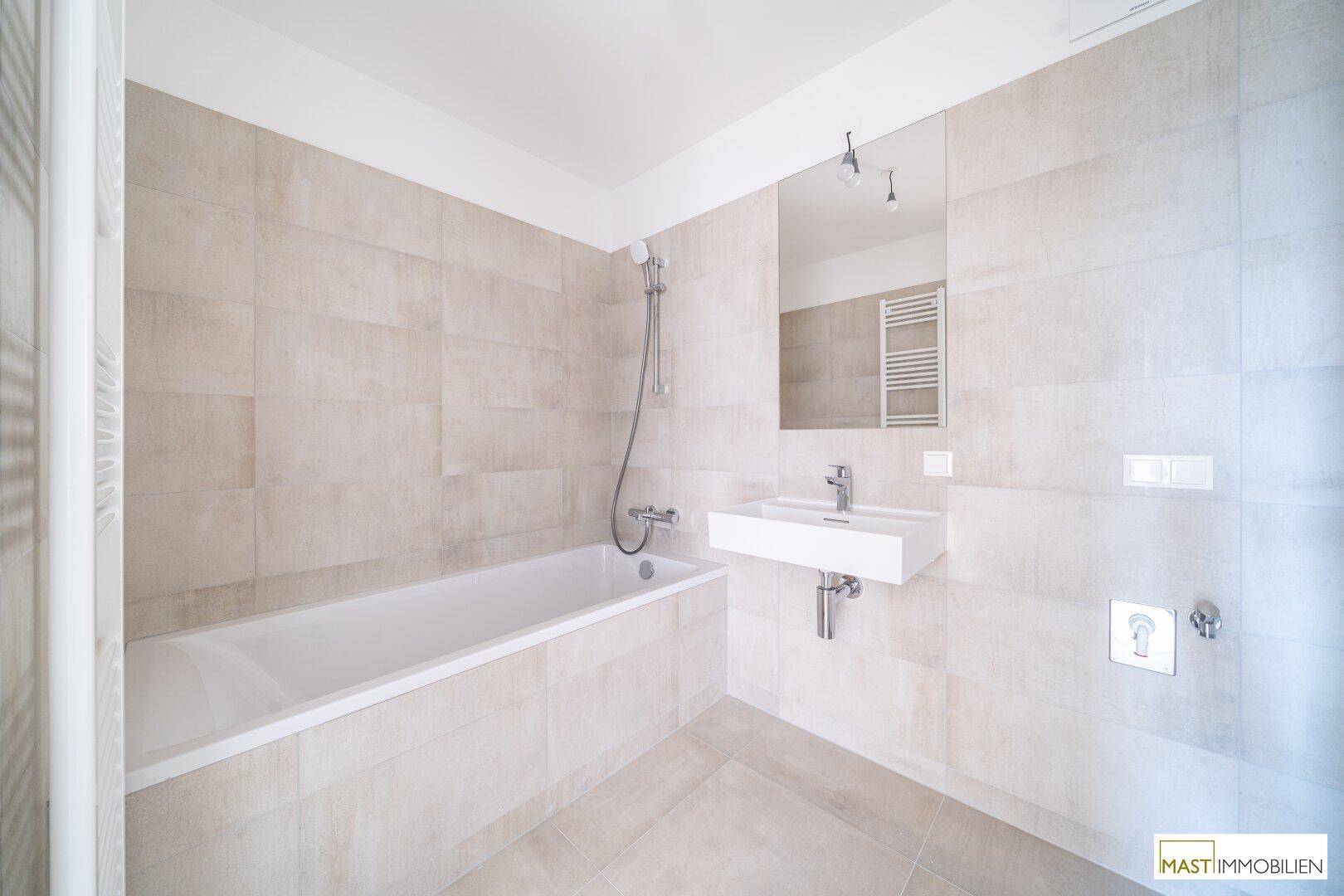 Helles Badezimmer mit Badewanne, modernem Waschbecken und beheiztem Handtuchhalter.