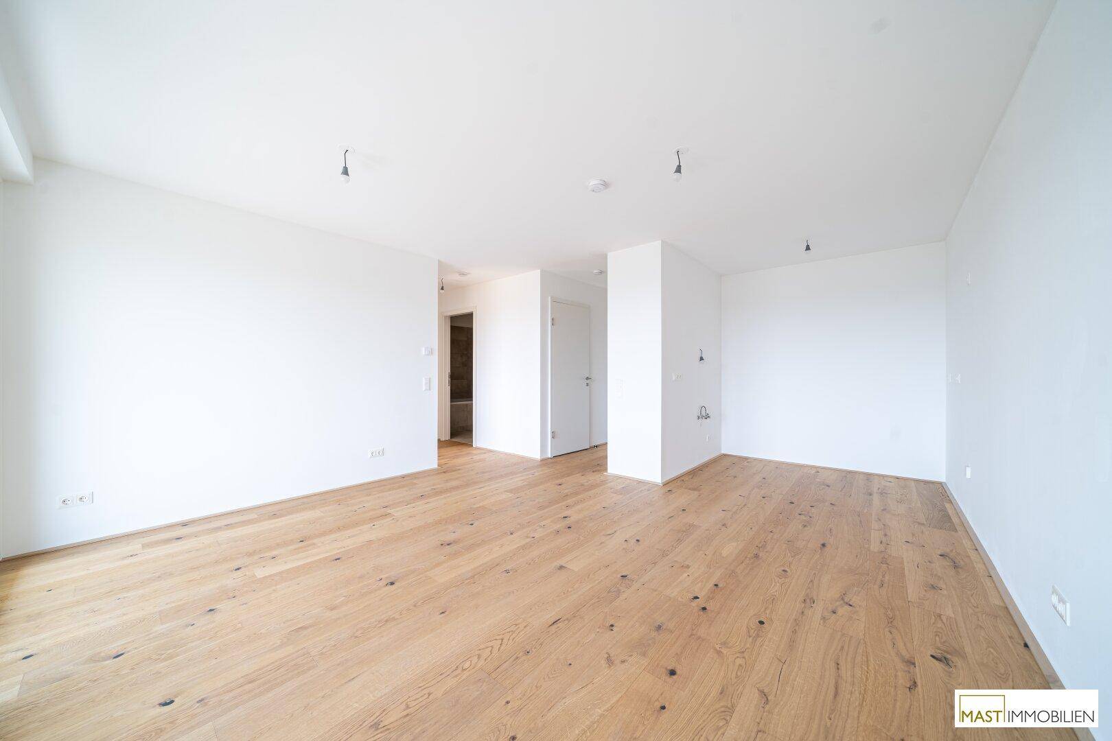 Geräumiger, heller Innenraum mit Holzboden und Zugang zu weiteren Zimmern.