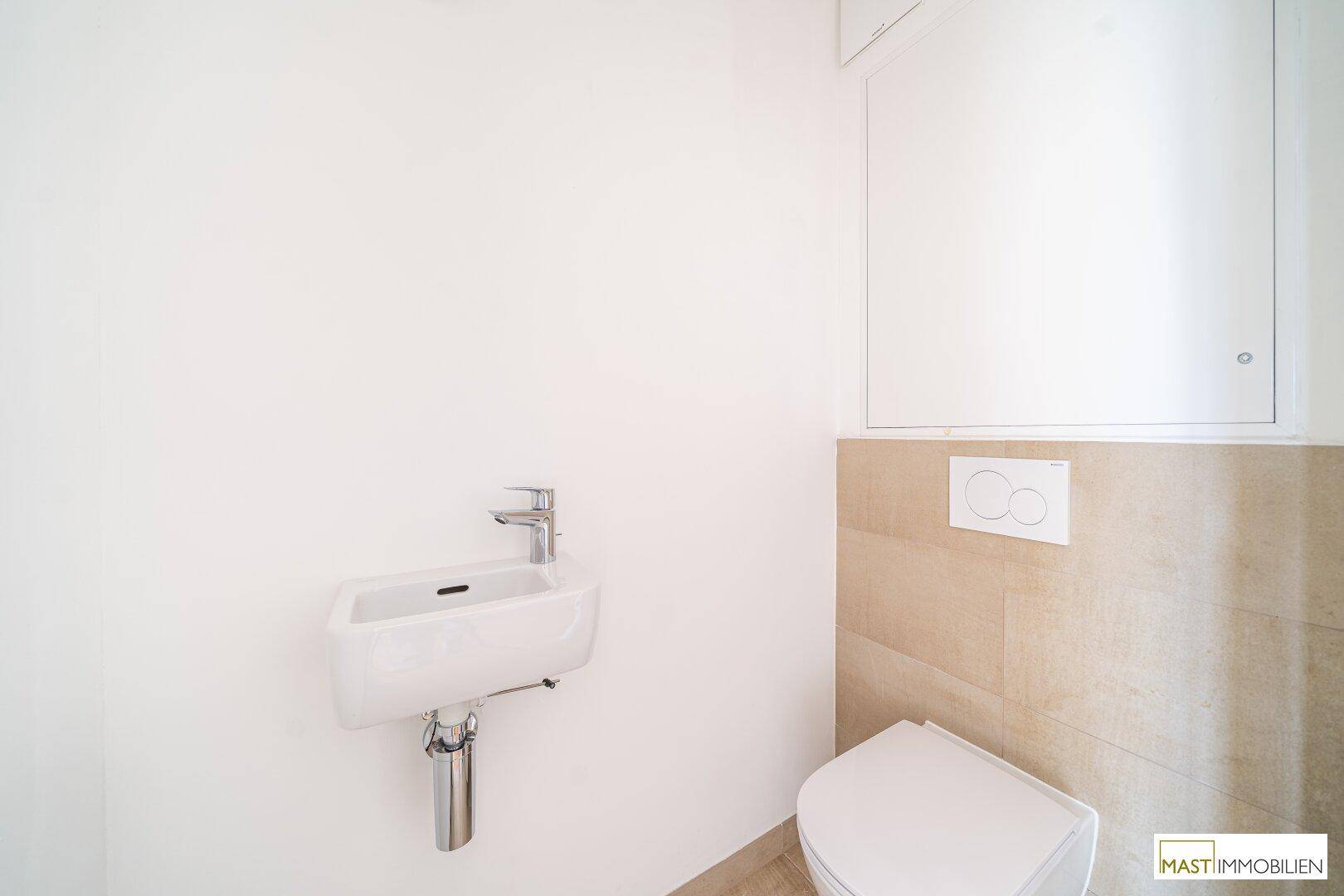 Modernes Gäste-WC mit wandhängender Toilette und kleinem Waschbecken in hellen Farbtönen.