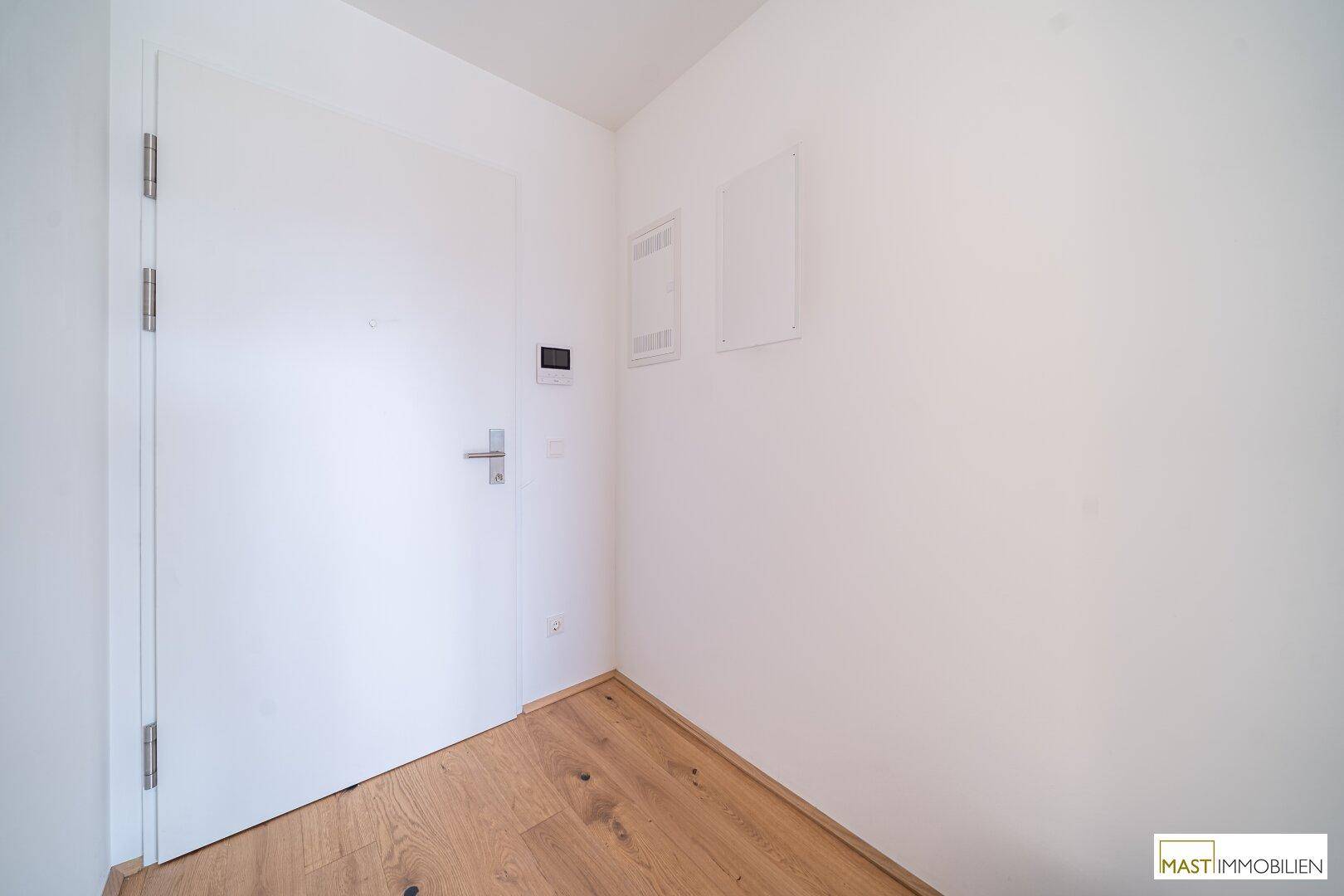 Heller Eingangsbereich mit weißer Tür und Holzboden, bereit für die individuelle Gestaltung.