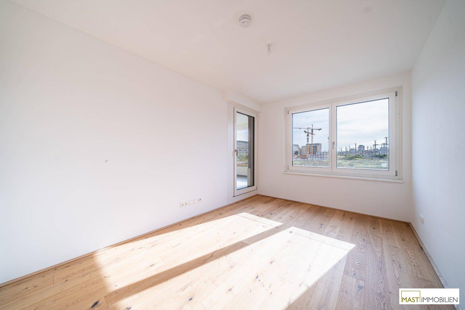 Lichtdurchflutetes Schlafzimmer mit Holzboden und Fenster mit Blick auf die Baustelle.