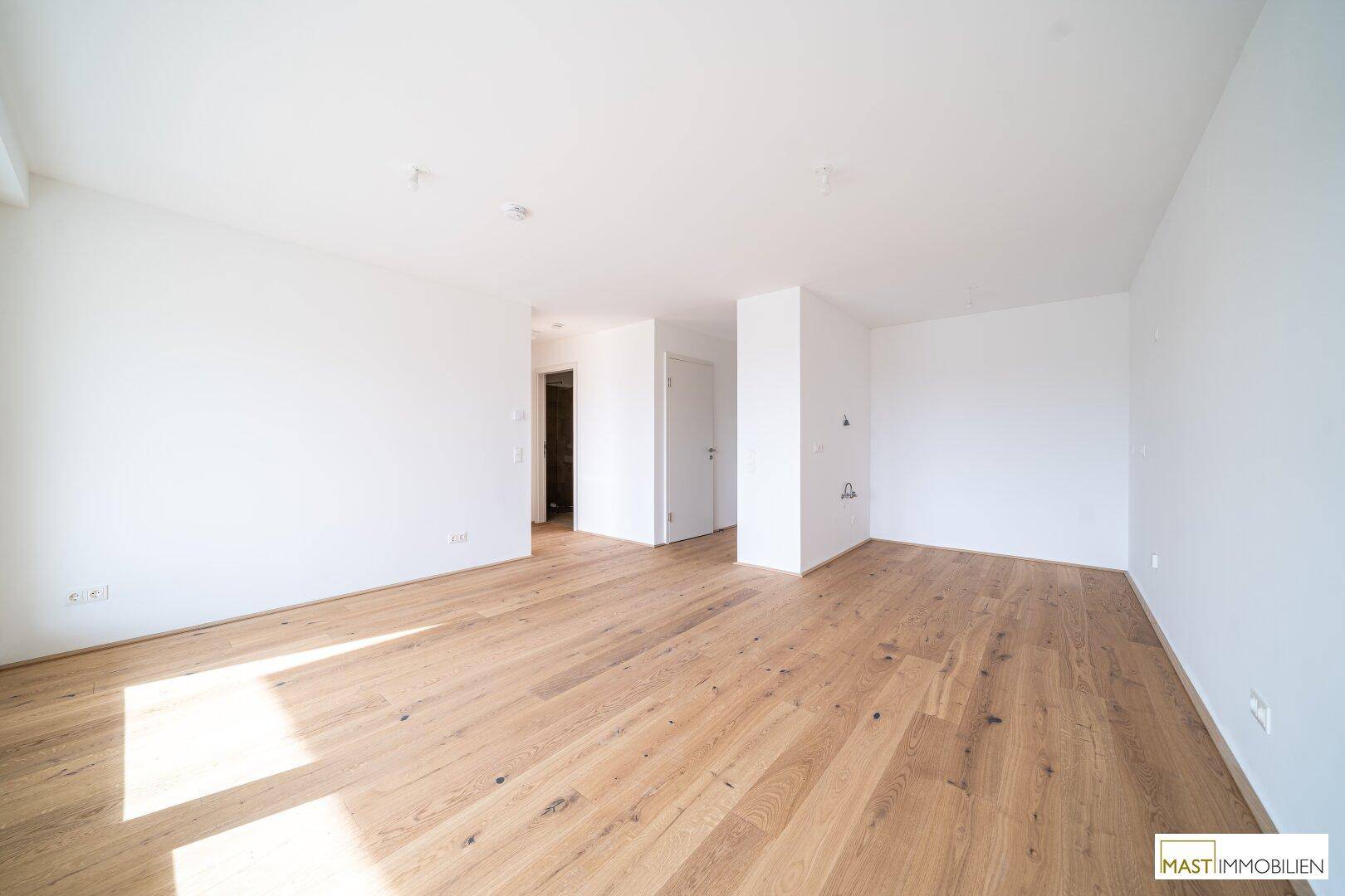 Großzügiger, heller Raum mit Holzboden und Zugang zu weiteren Zimmern, ideal für offenes Wohnen.