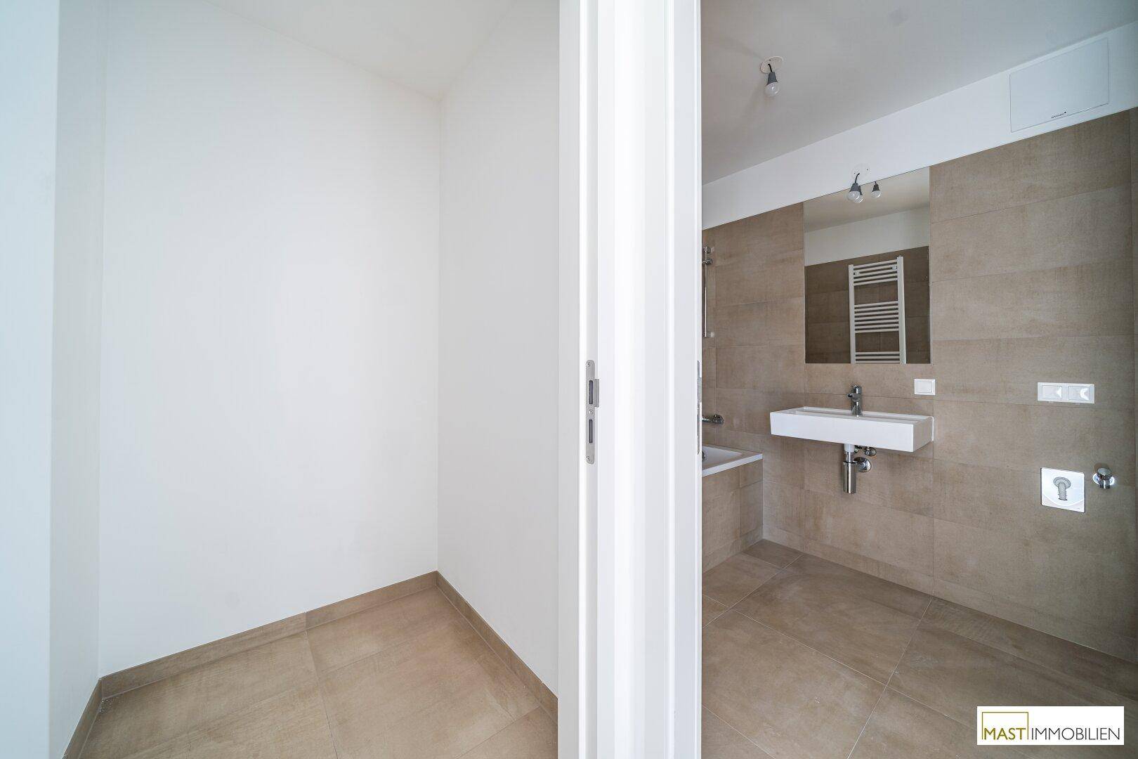 Blick in ein modernes Badezimmer mit beigefarbenen Fliesen und weißer Tür.