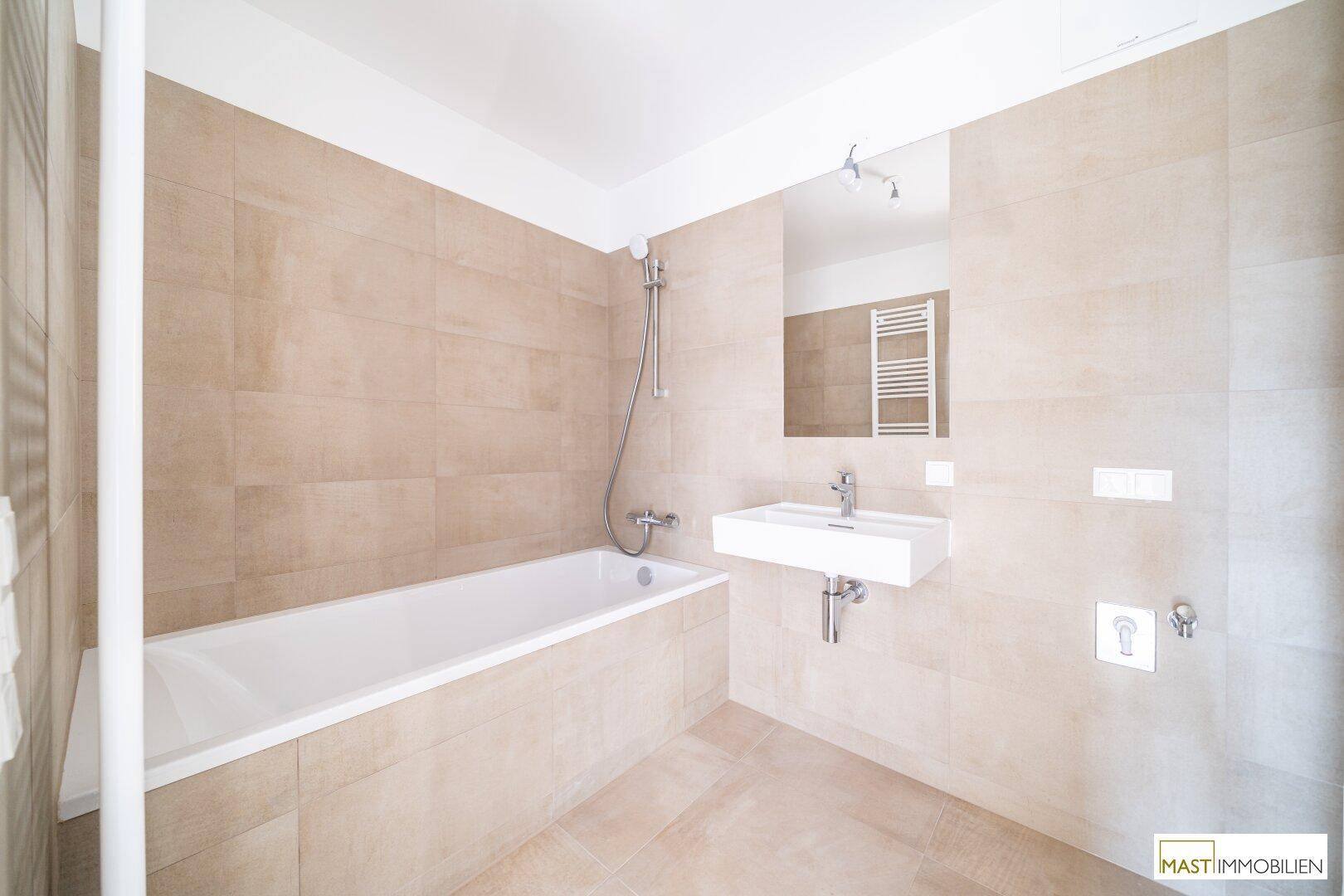 Modernes Badezimmer mit Badewanne, Waschbecken und beigefarbenen Wand- und Bodenfliesen.