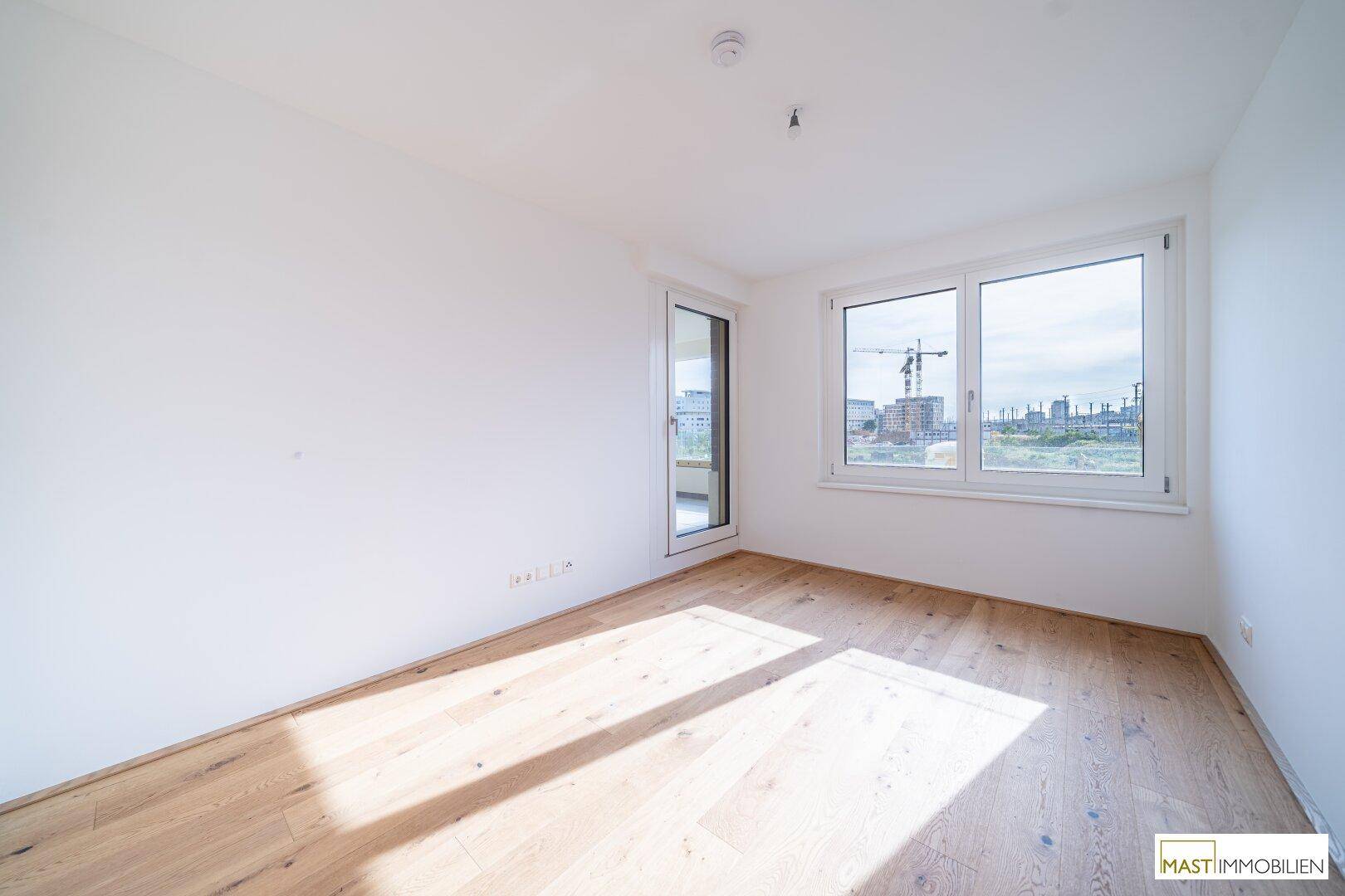Leeres Schlafzimmer mit hellem Eichenparkettboden und Fenster mit Blick auf die Umgebung.
