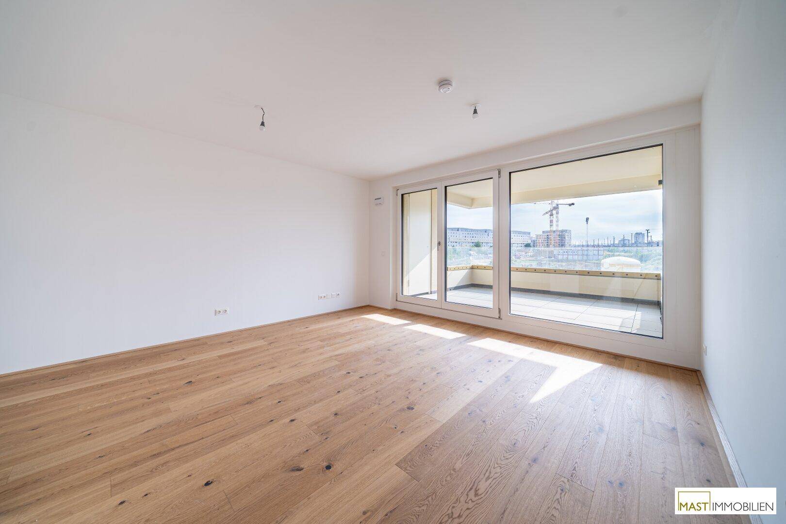 Helles, leeres Zimmer mit Eichenparkettboden und Zugang zu einem großen Balkon.