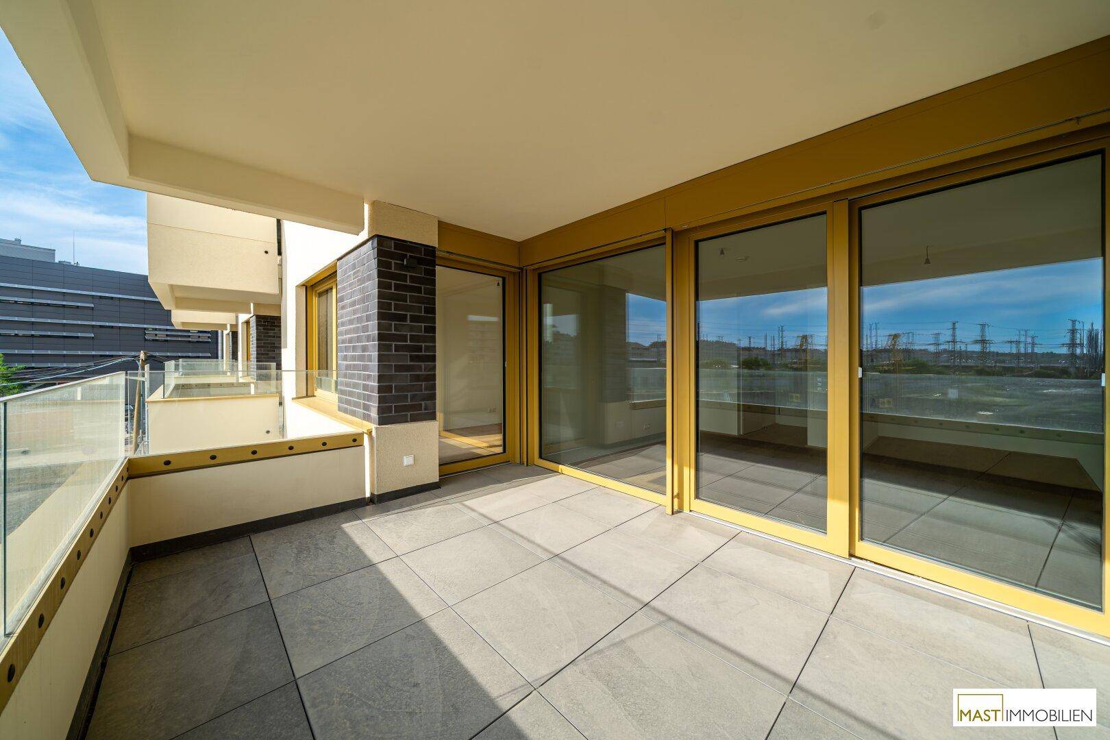 Breiter Balkon mit modernen Fliesen und großen Glasfronten, die viel Licht in die Innenräume lassen.