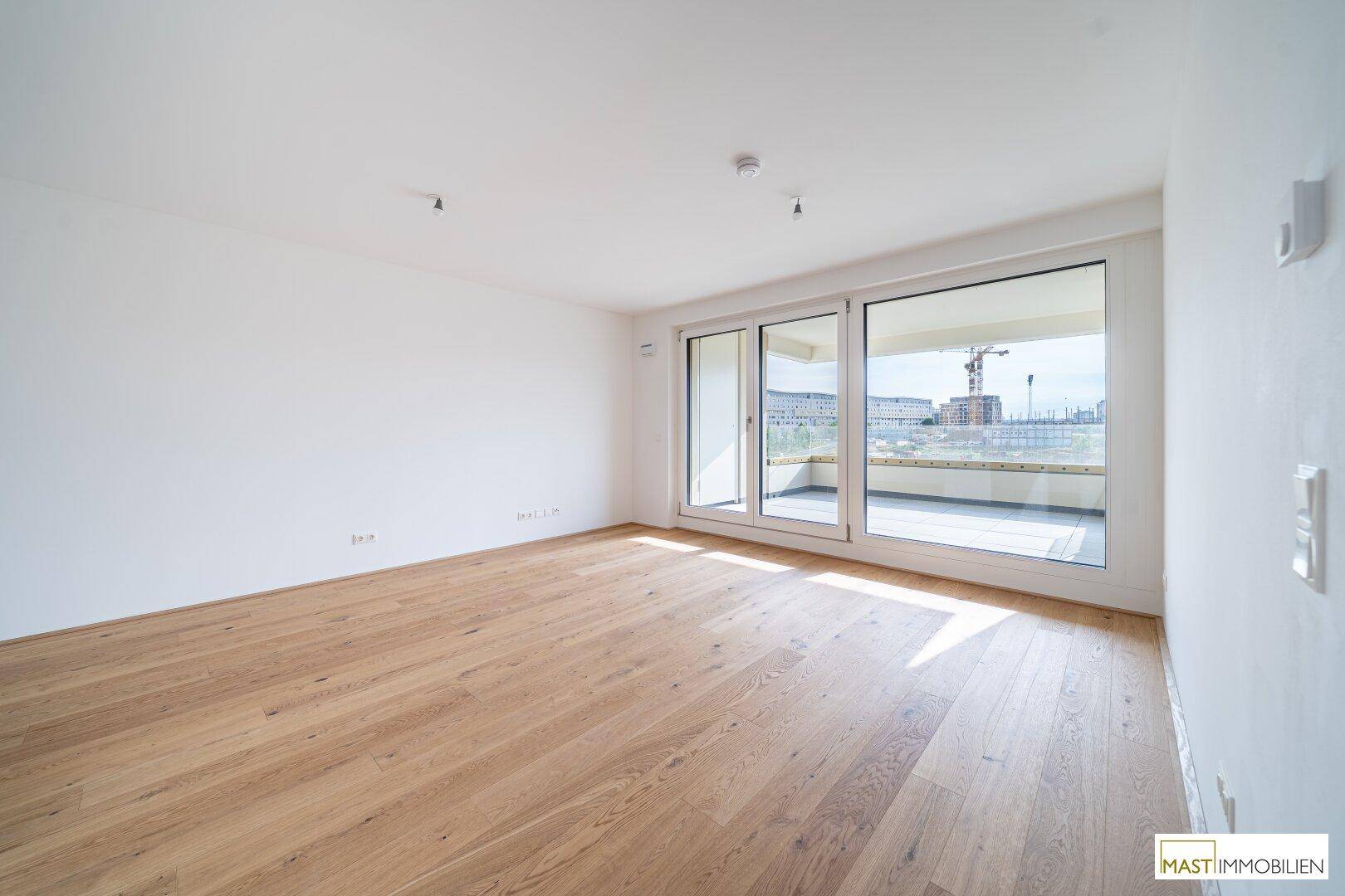 Helles, leeres Zimmer mit Eichenparkett und großen Schiebetüren, die auf einen Balkon führen.