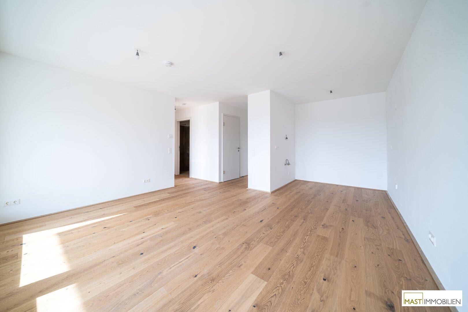 Geräumiges, leeres Zimmer mit hellem Parkettboden und weiß gestrichenen Wänden, bereit zur Einrichtung.