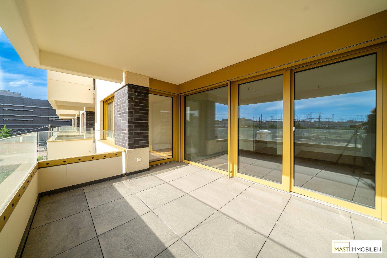 Breiter Balkon mit Fliesenboden und großen Glasfronten, die viel Licht in die angrenzenden Räume lassen.