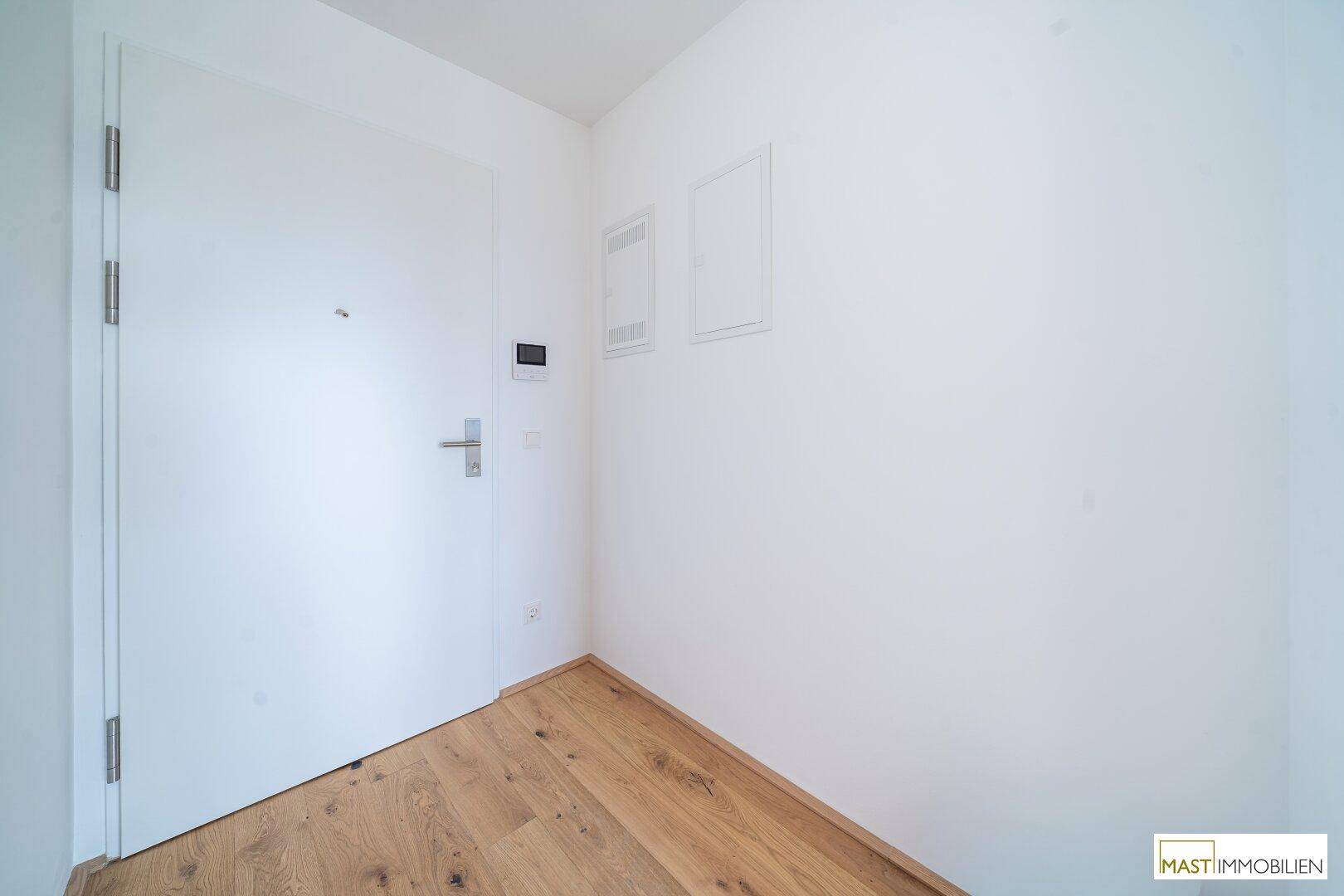 Heller Eingangsbereich mit Holzboden und weißer Tür, einladend und funktional gestaltet.