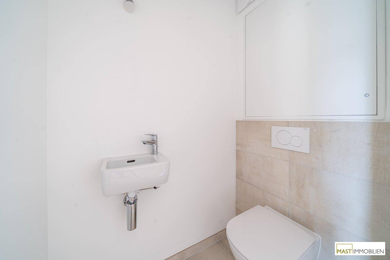 Separates Gäste-WC mit wandhängender Toilette und kleinem Waschbecken, in schlichtem Design.