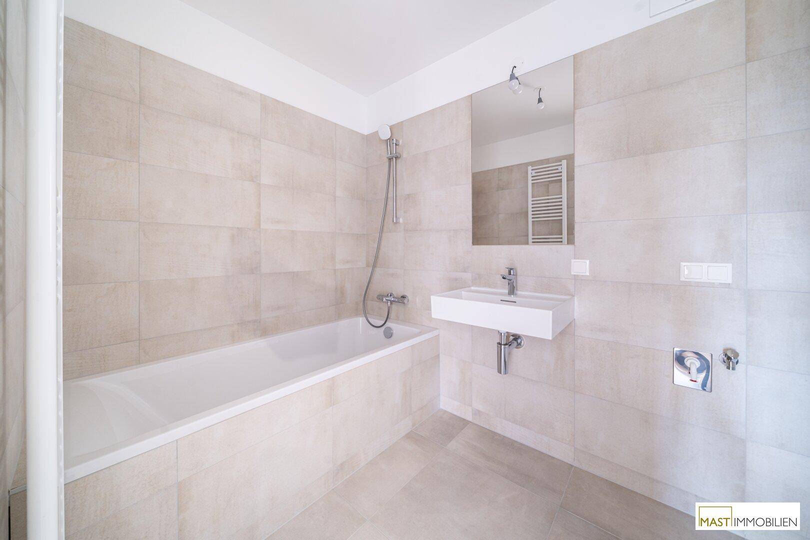 Modernes Badezimmer mit Badewanne, Waschbecken und hellen Fliesen, in neuwertigem Zustand.