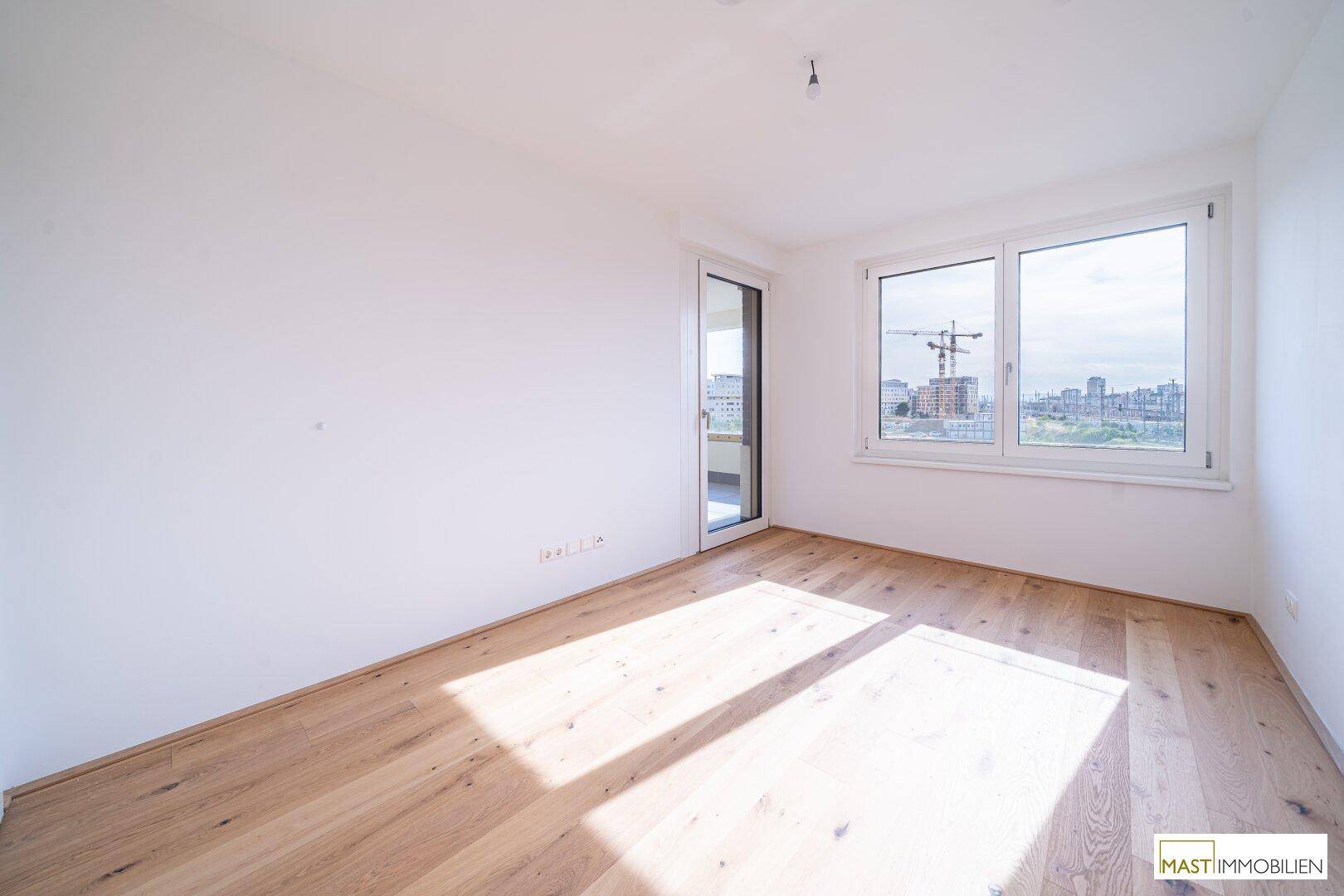 Helles Schlafzimmer mit Holzboden und Zugang zum Balkon, bietet viel Tageslicht.