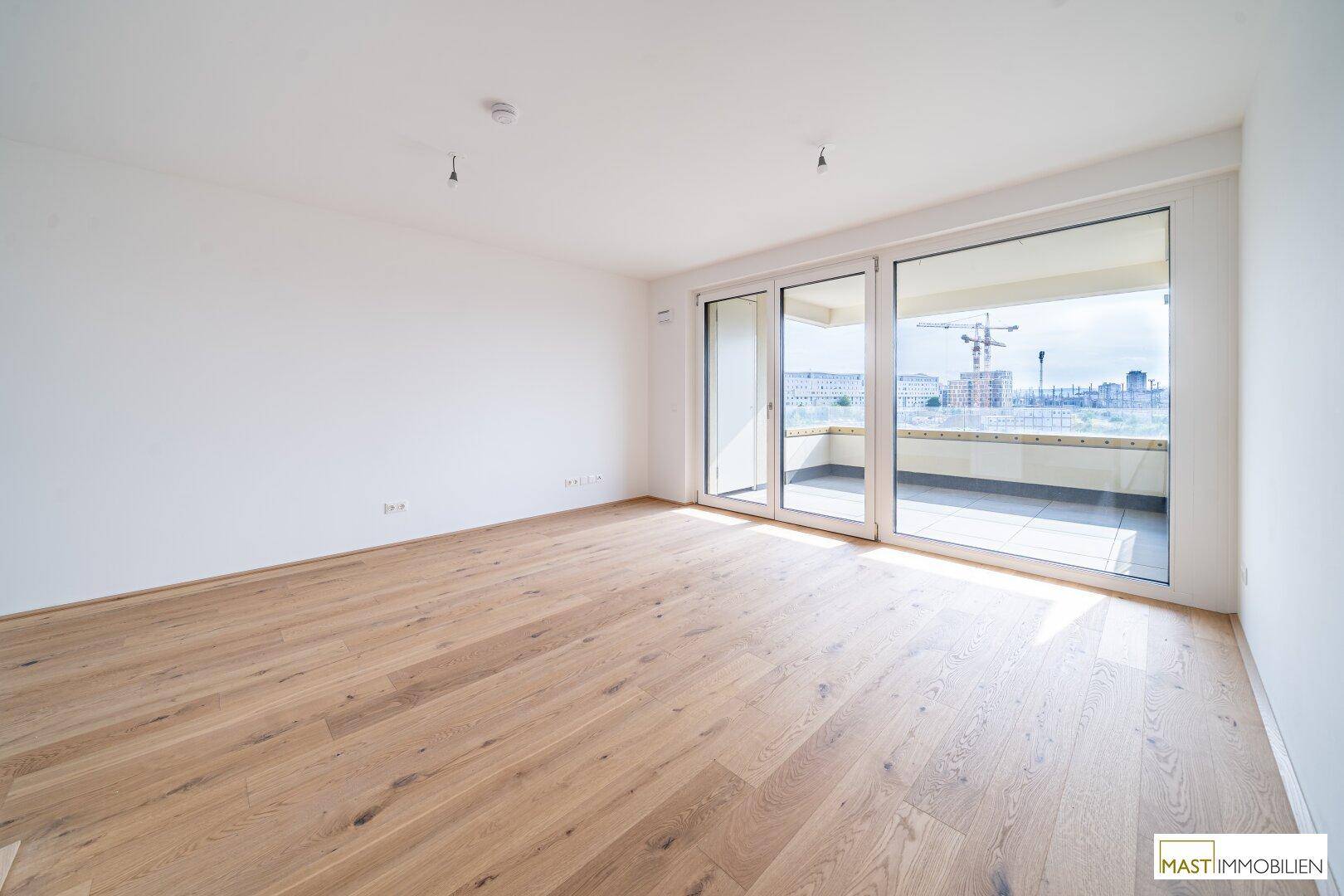 Heller Wohnbereich mit Holzboden und großen Schiebetüren zum Balkon, ideal für offenes Wohnen.