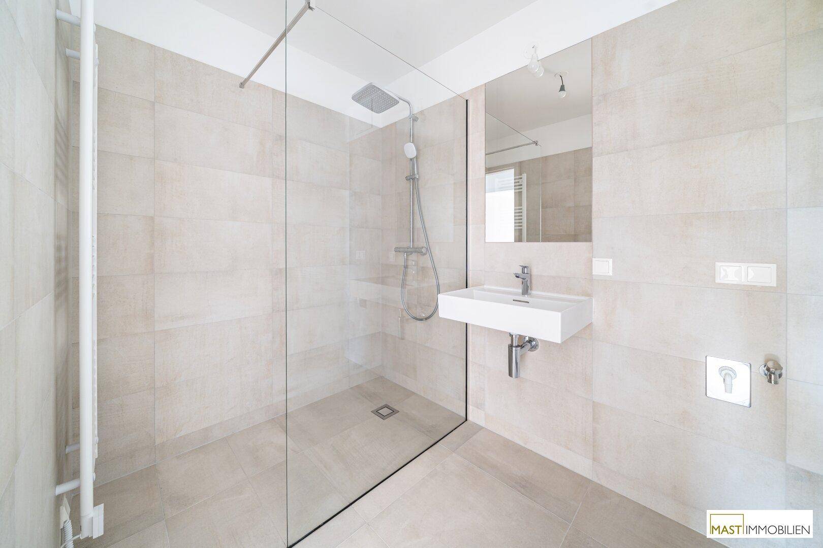 Modernes Badezimmer mit ebenerdiger Dusche, Wandwaschbecken und hellen Fliesen.