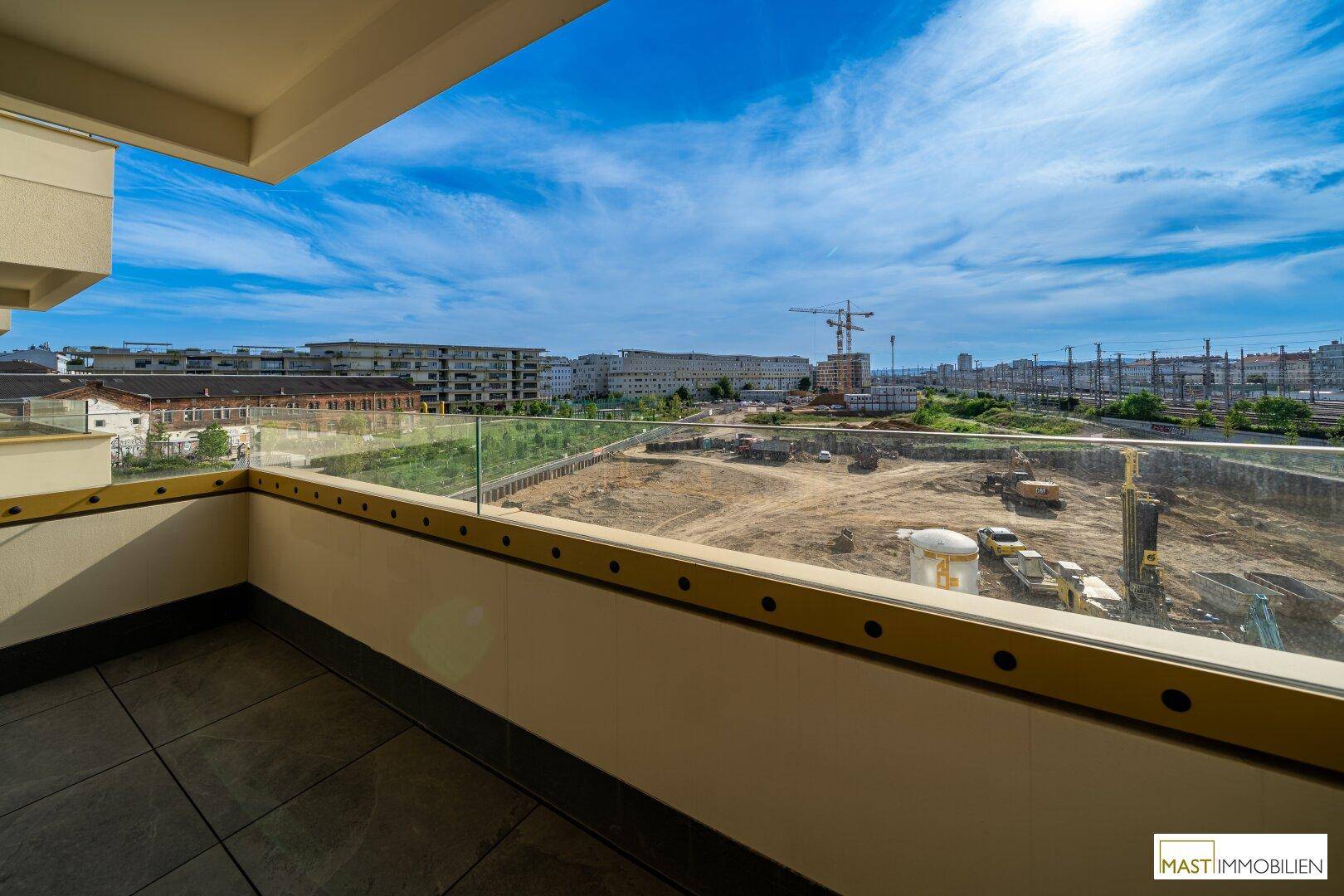 Balkon mit Glasbrüstung und weitem Blick auf eine Baustelle und die städtische Landschaft.