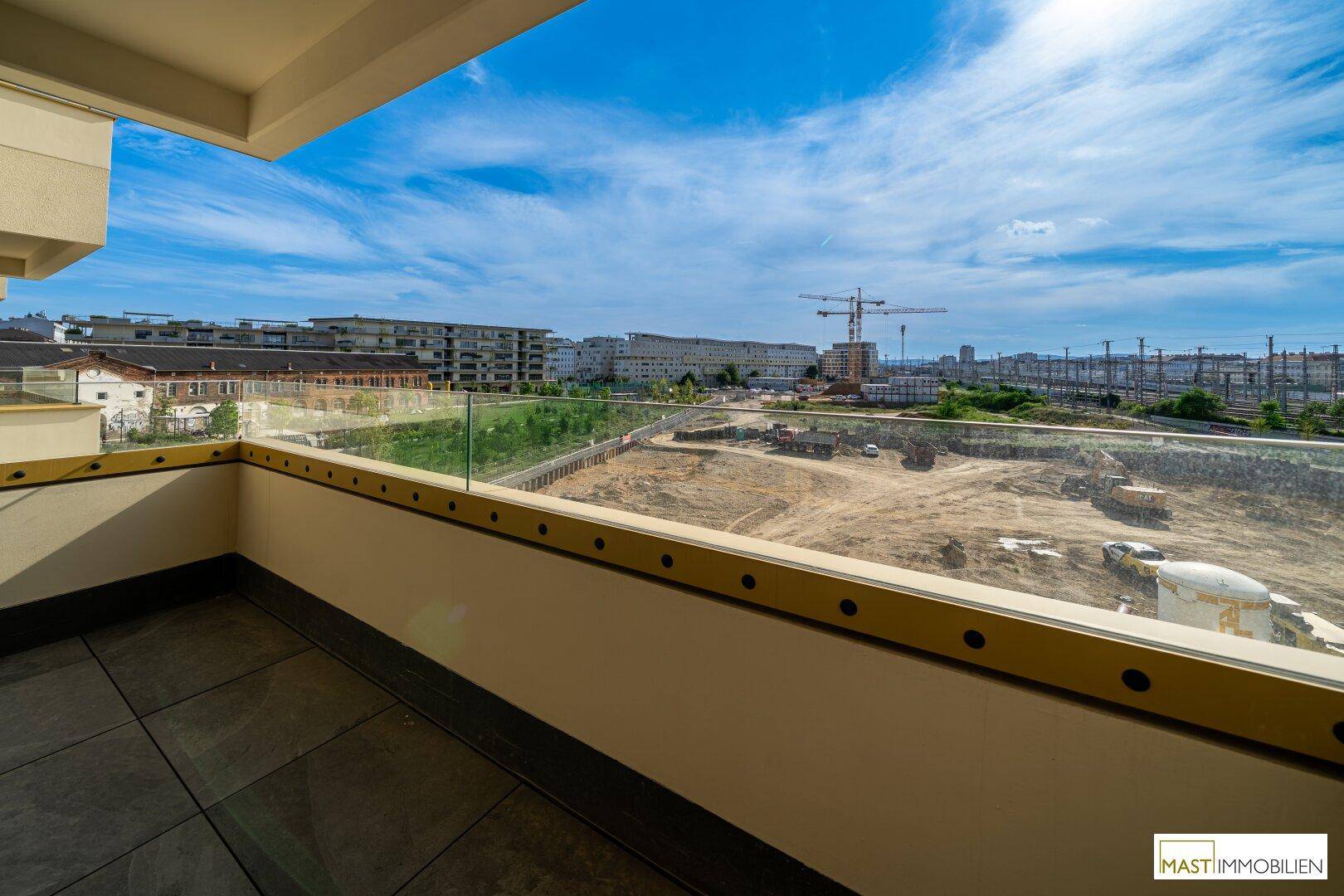 Weitläufiger Blick vom Balkon auf die Stadt und eine Baustelle unter blauem Himmel.