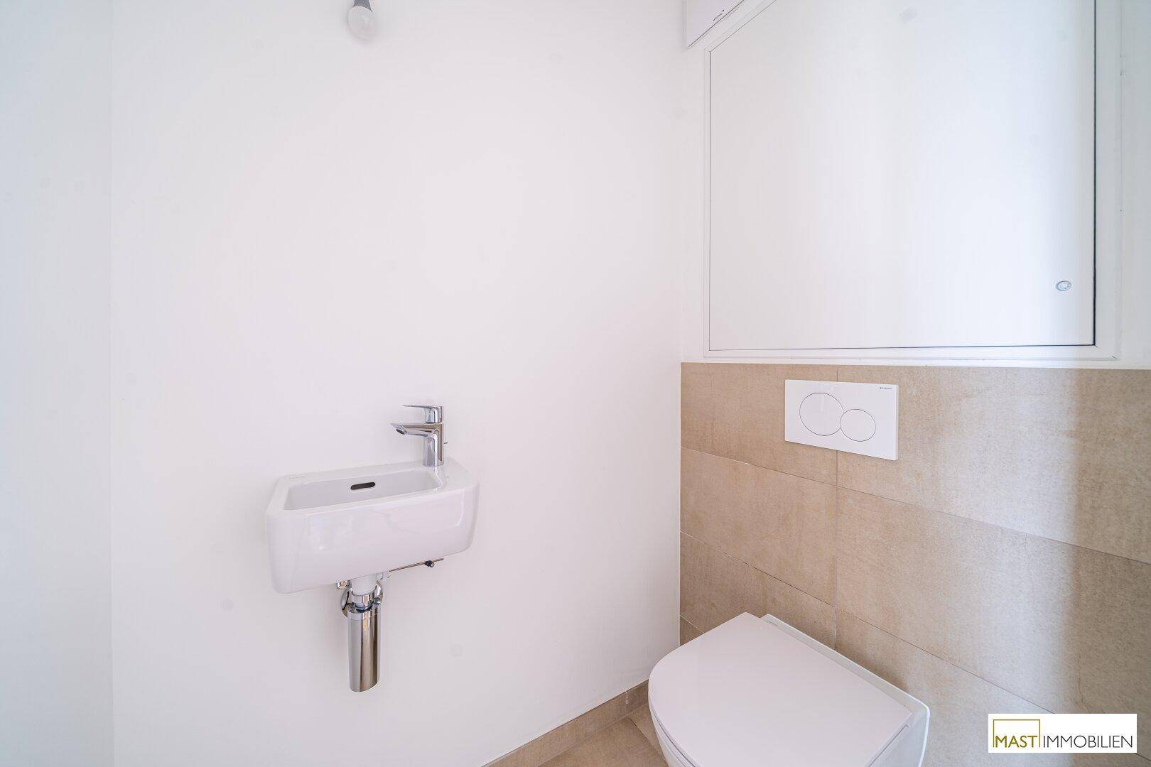 Modernes Gäste-WC mit wandhängender Toilette, kleinem Waschbecken und beigefarbenen Fliesen.