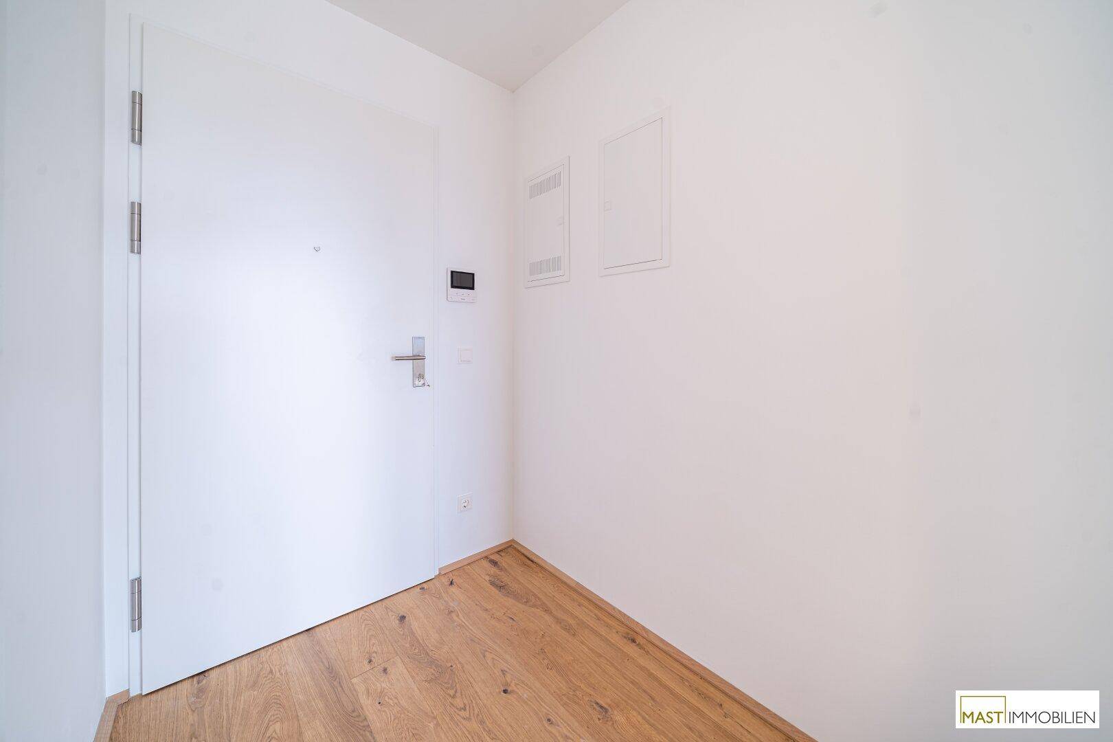 Heller Eingangsbereich mit weißer Tür und hochwertigem Holzboden.