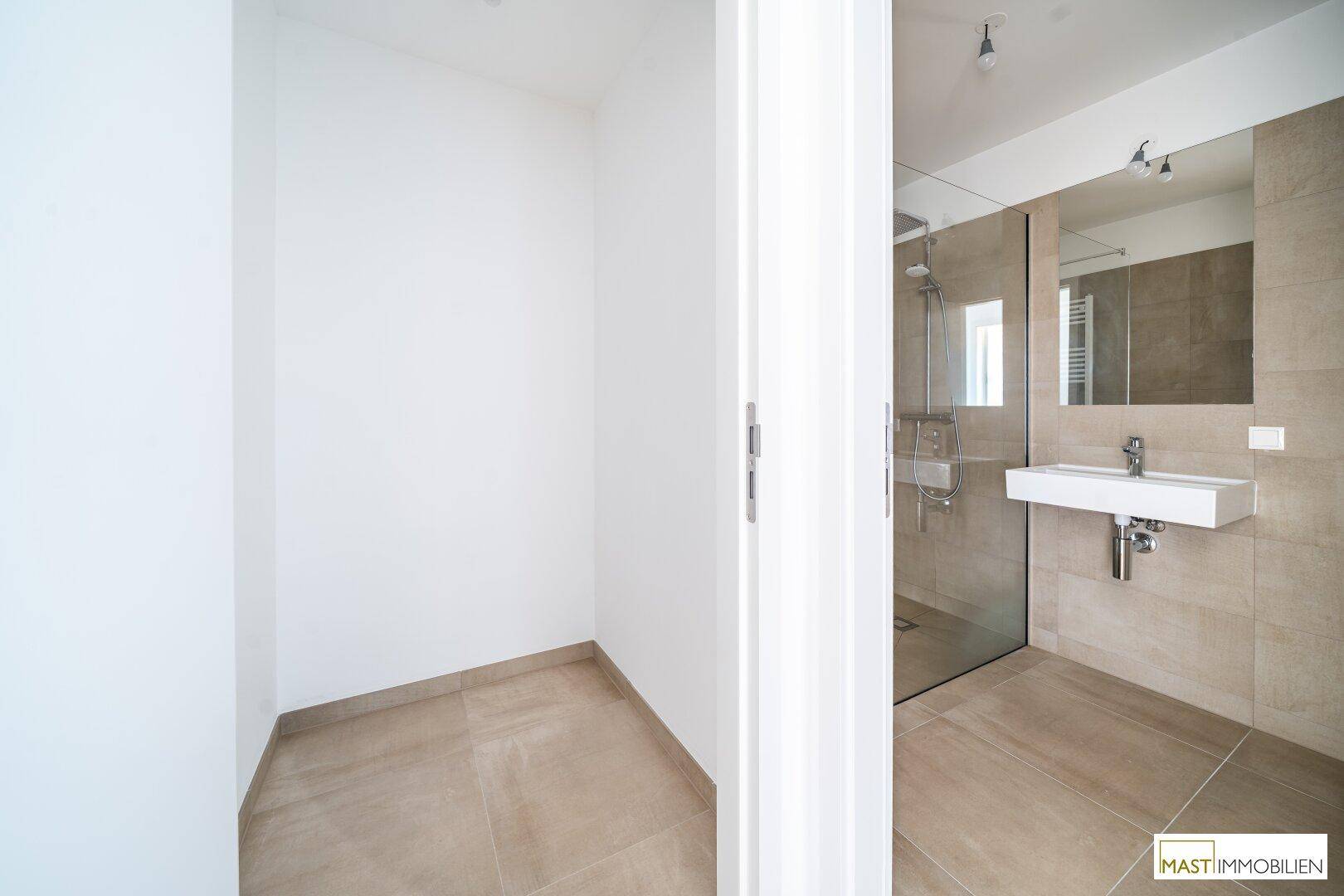 Blick in einen kleinen Abstellraum und ein modernes Badezimmer mit Dusche.