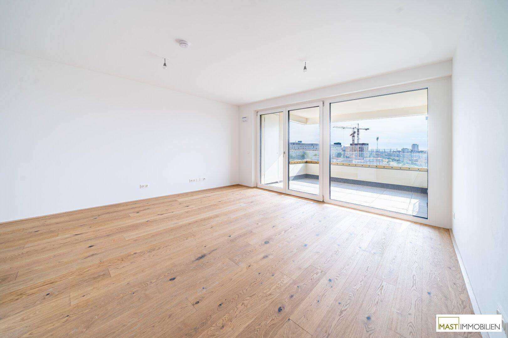Geräumiger, heller Raum mit Holzboden und großen Glasschiebetüren zum Außenbereich.