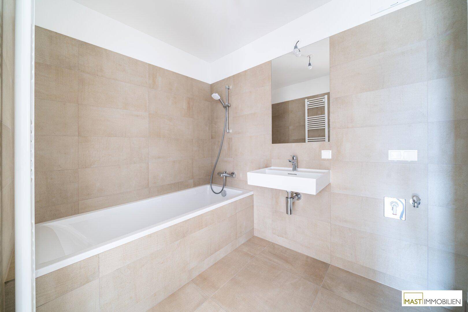 Modernes Badezimmer mit Badewanne, Einzelwaschbecken, beheiztem Handtuchhalter und beigefarbenen Fliesen.