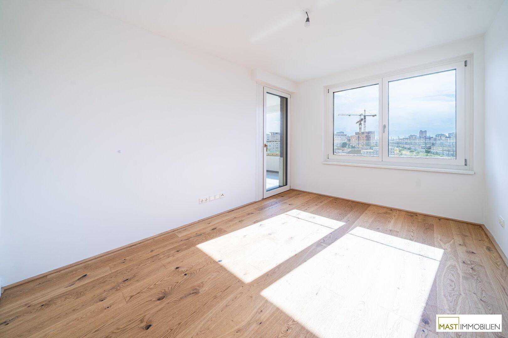 Helles Schlafzimmer mit Holzboden, großem Fenster und Balkonzugang, mit Blick auf die Stadt.
