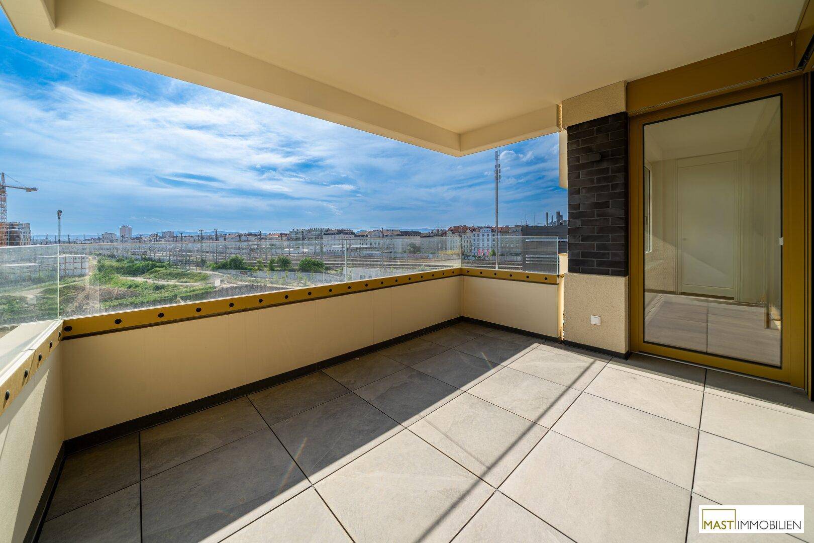 Großer Balkon mit Fliesenboden und Glasbrüstung, bietet einen weiten Blick über Baustellen und die Stadt.