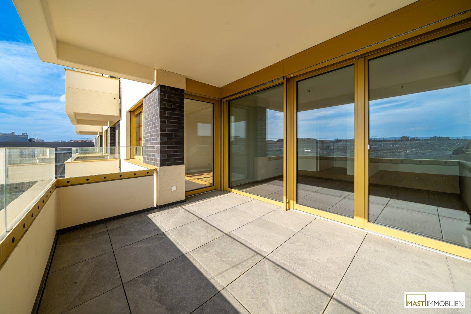 Geräumiger Balkon mit Fliesenboden und Glasgeländer, bietet einen weiten Blick auf die Umgebung.