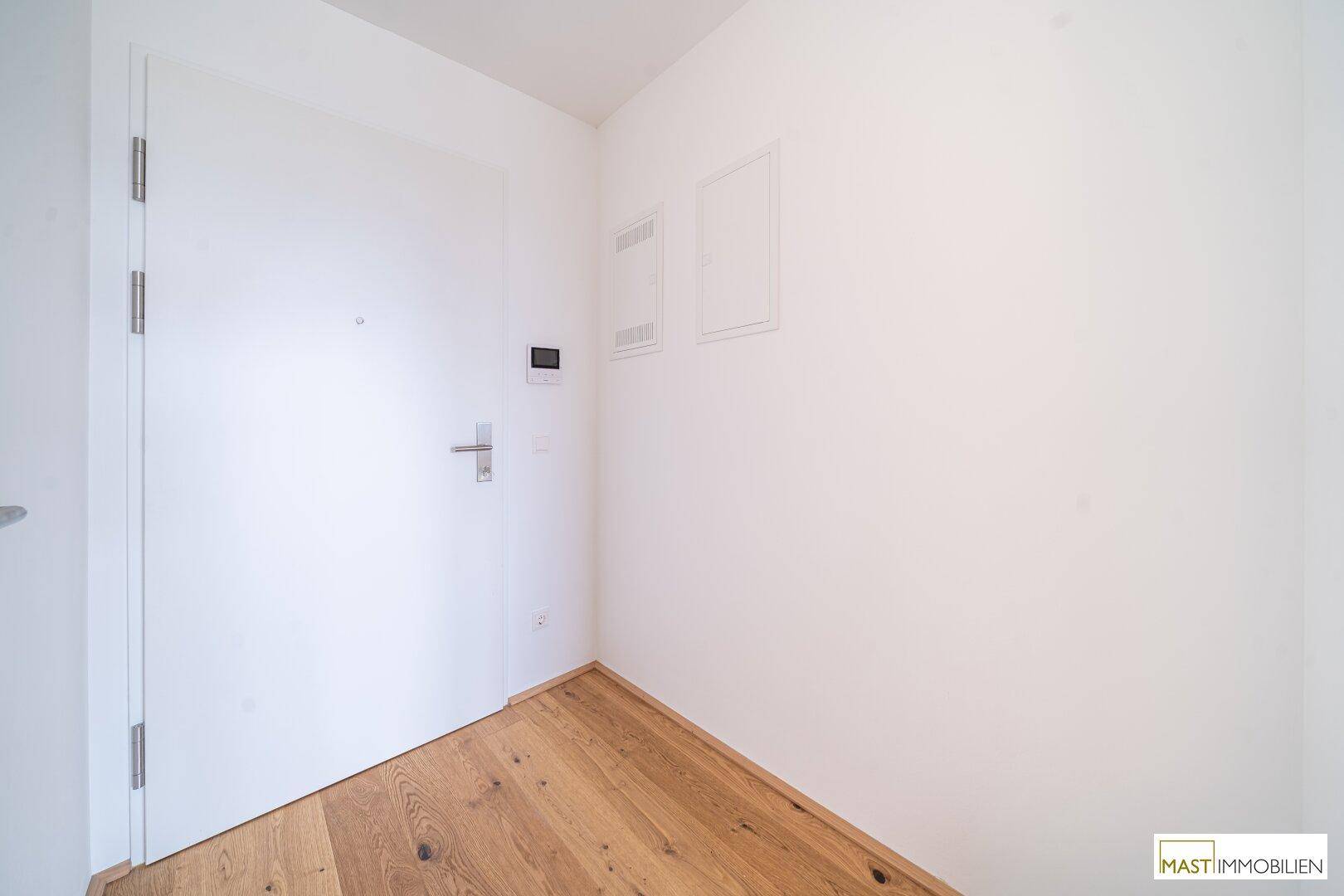 Eingangsbereich mit Holzboden und weißer Tür, deutet auf Neubau hin.