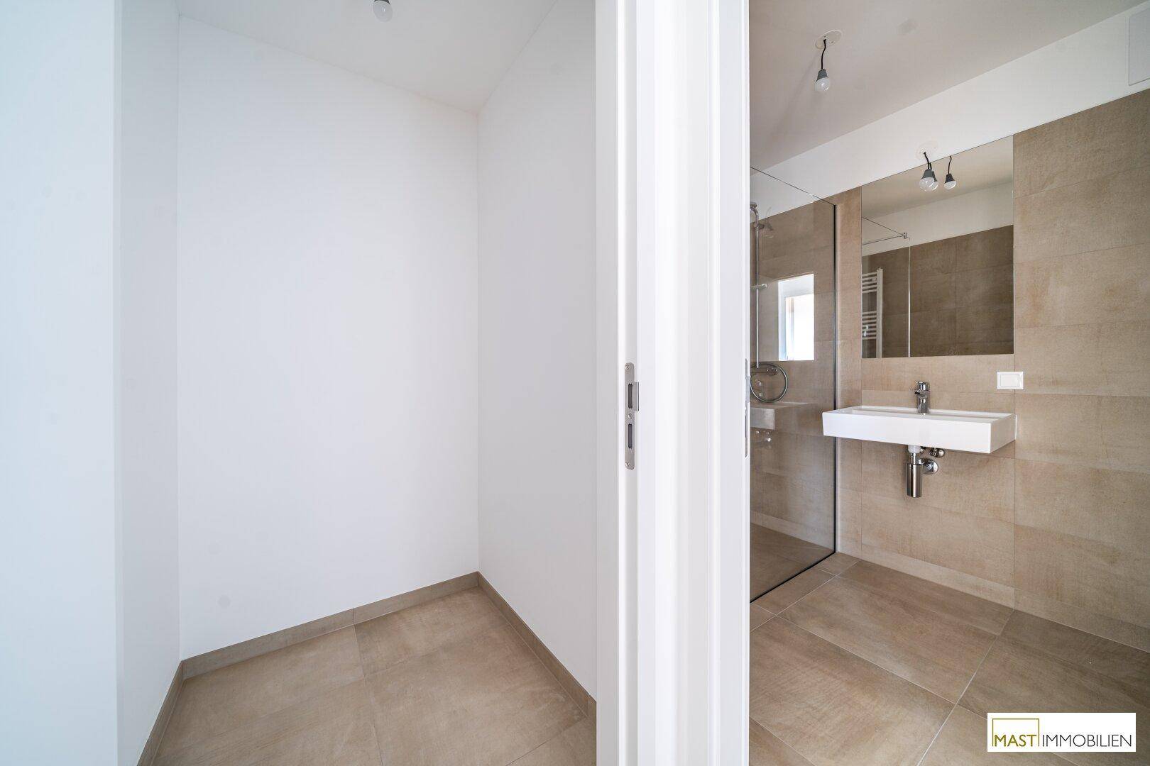 Modernes Badezimmer mit beigefarbenen Fliesen und einem separaten Abstellraum.