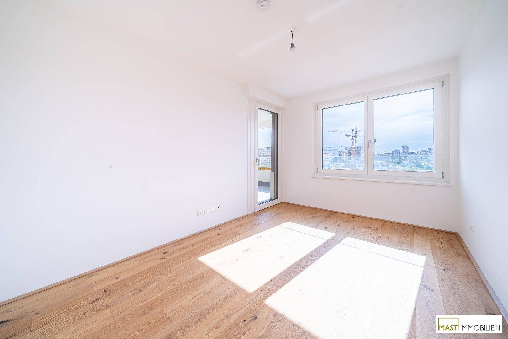 Lichtdurchfluteter Raum mit Parkettboden und Blick auf die Stadt durch große Fenster.