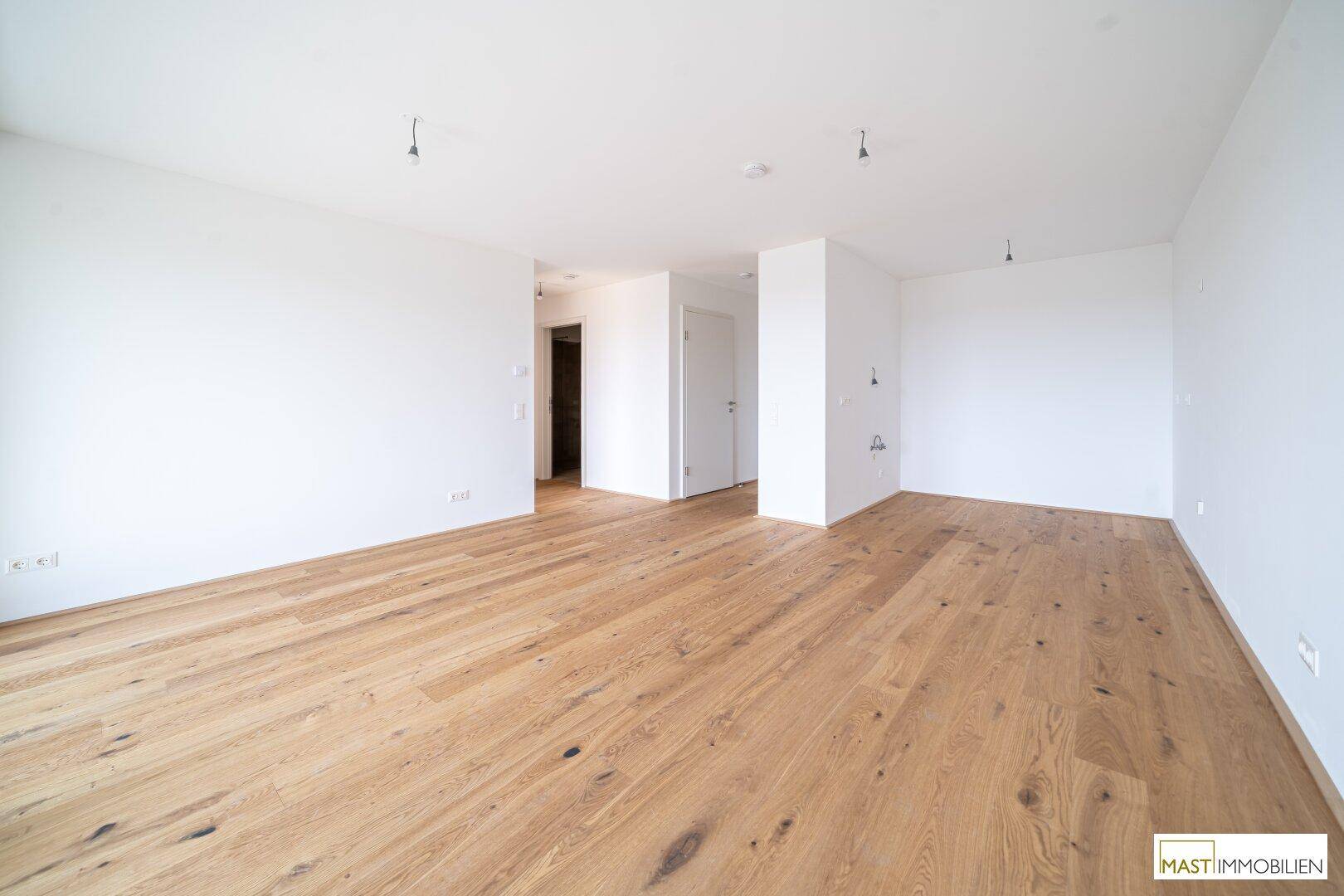 Geräumiger, heller Raum mit Holzboden und Zugang zu weiteren Zimmern.