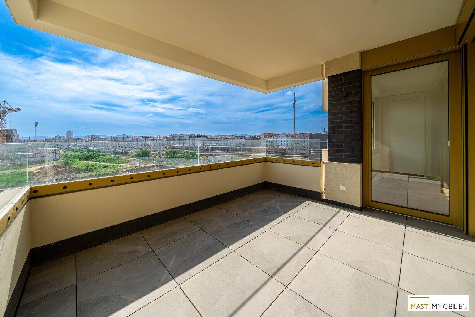 Großer Balkon mit Fliesenboden und Glasbrüstung, bietet weite Aussicht.