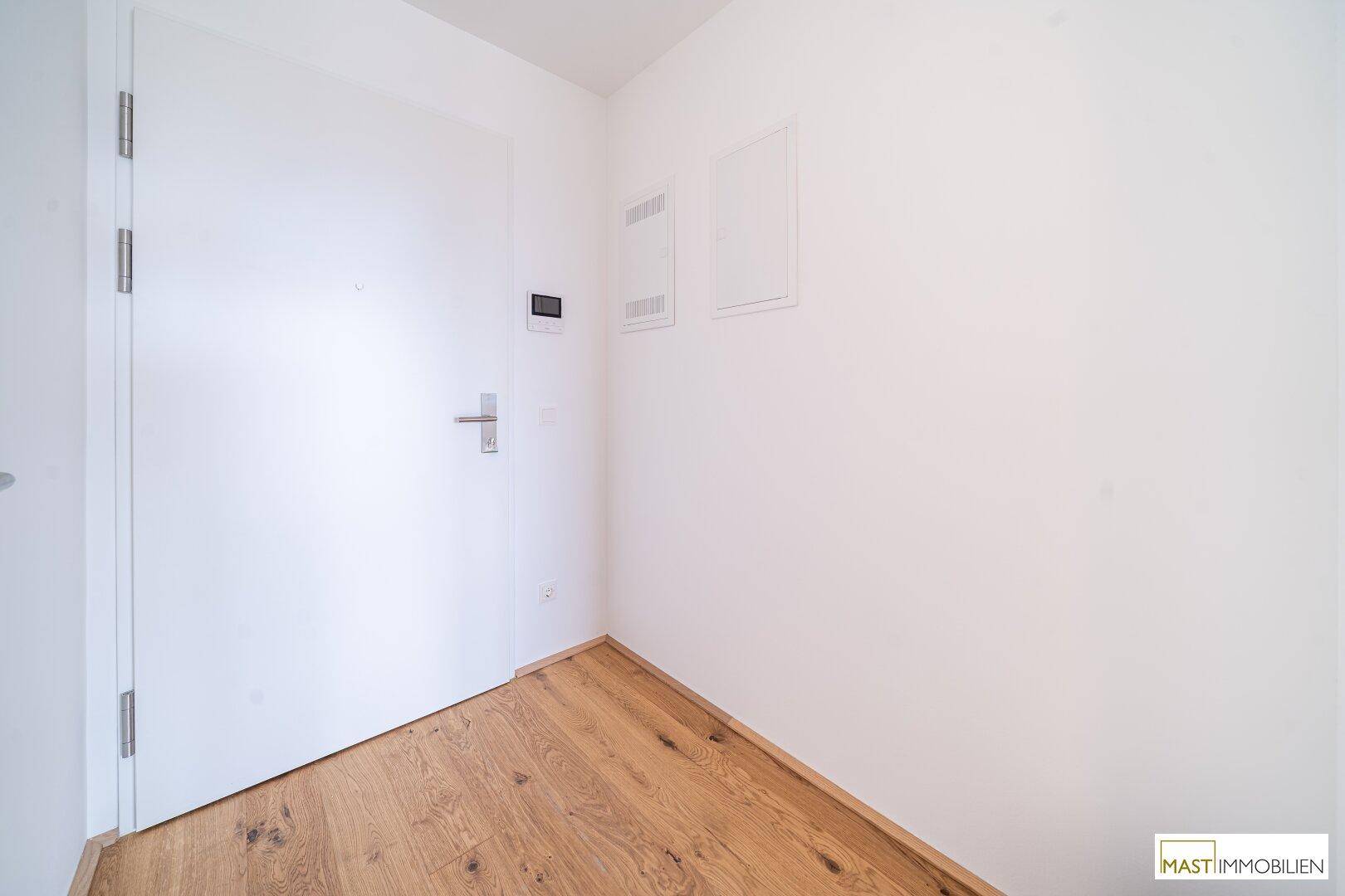 Heller Eingangsbereich mit Holzboden und moderner weißer Tür, die zur Wohnung führt.