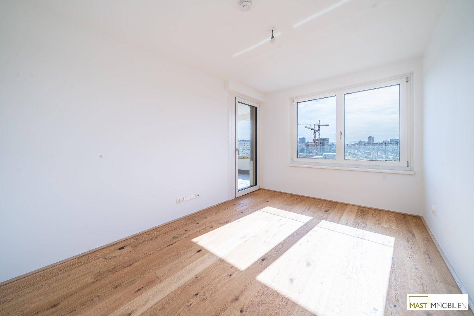 Helles Zimmer mit Eichenparkett, großen Fenstern und Zugang zu einem Außenbereich mit Stadtblick.