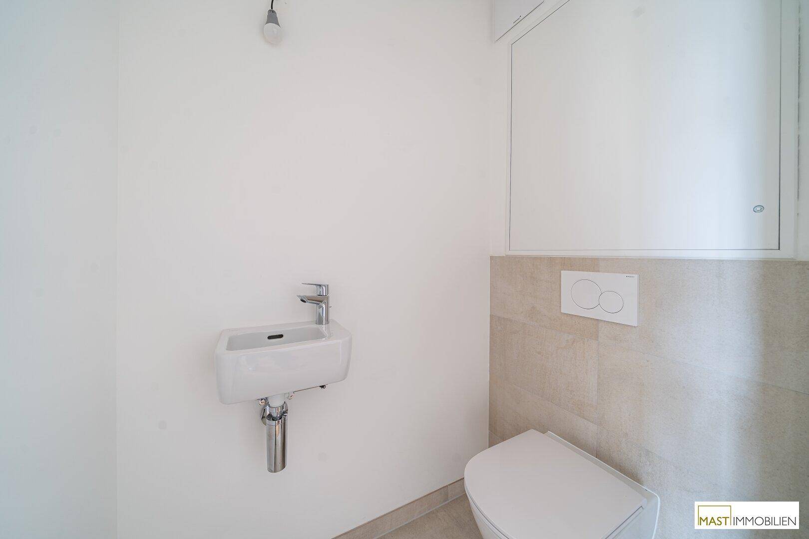 Separates WC mit wandhängender Toilette und kleinem Waschbecken, in schlichtem Design gehalten.