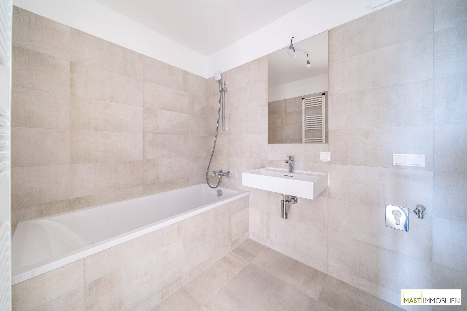 Modernes Badezimmer mit Badewanne, Waschbecken und hellen Fliesen, ausgestattet mit Handtuchheizkörper.
