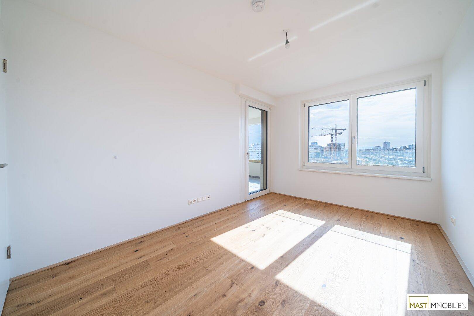 Lichtdurchflutetes Zimmer mit Holzboden und großen Fenstern, ideal als Schlafzimmer nutzbar.