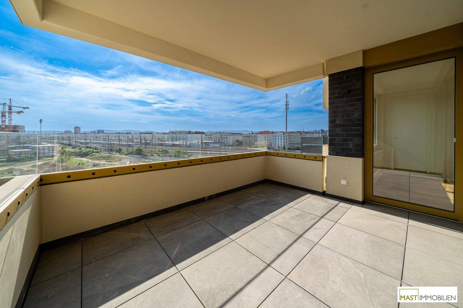 Geräumiger Balkon mit Fliesenboden und Glasbrüstung, bietet einen weiten Blick über die Stadt.