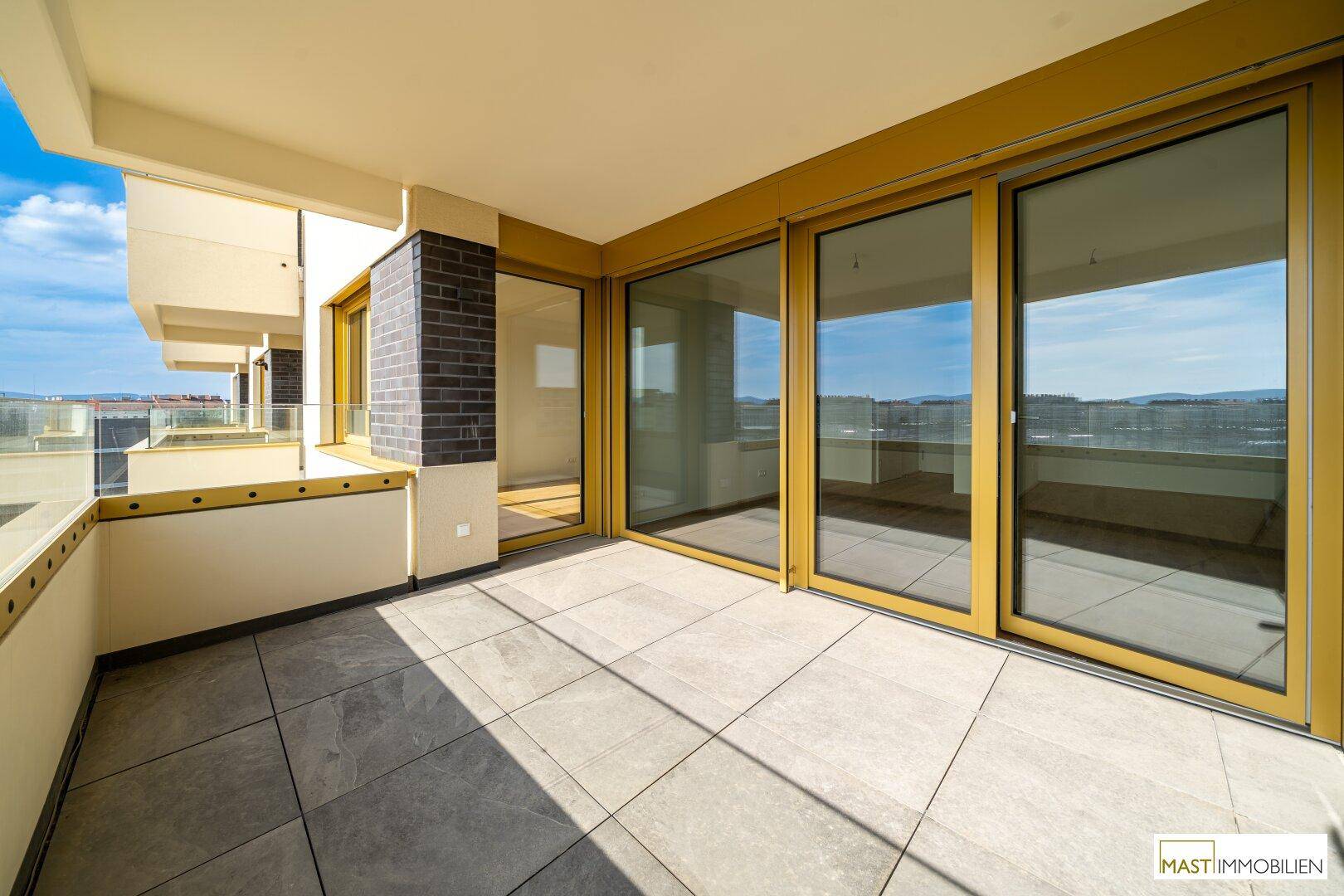 Breiter Balkon mit Schiebetüren und Fliesenboden, bietet viel Platz und eine offene Aussicht.