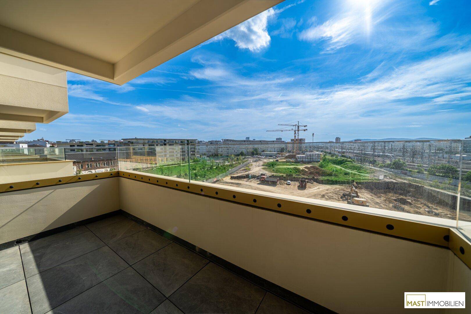 Sonniger Balkon mit Glasbrüstung und weitem Blick über die Stadt und Baustellen.